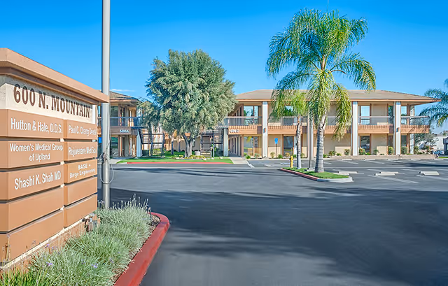 Front view of a senior living campus with beige buildings, palm trees, and a sign.