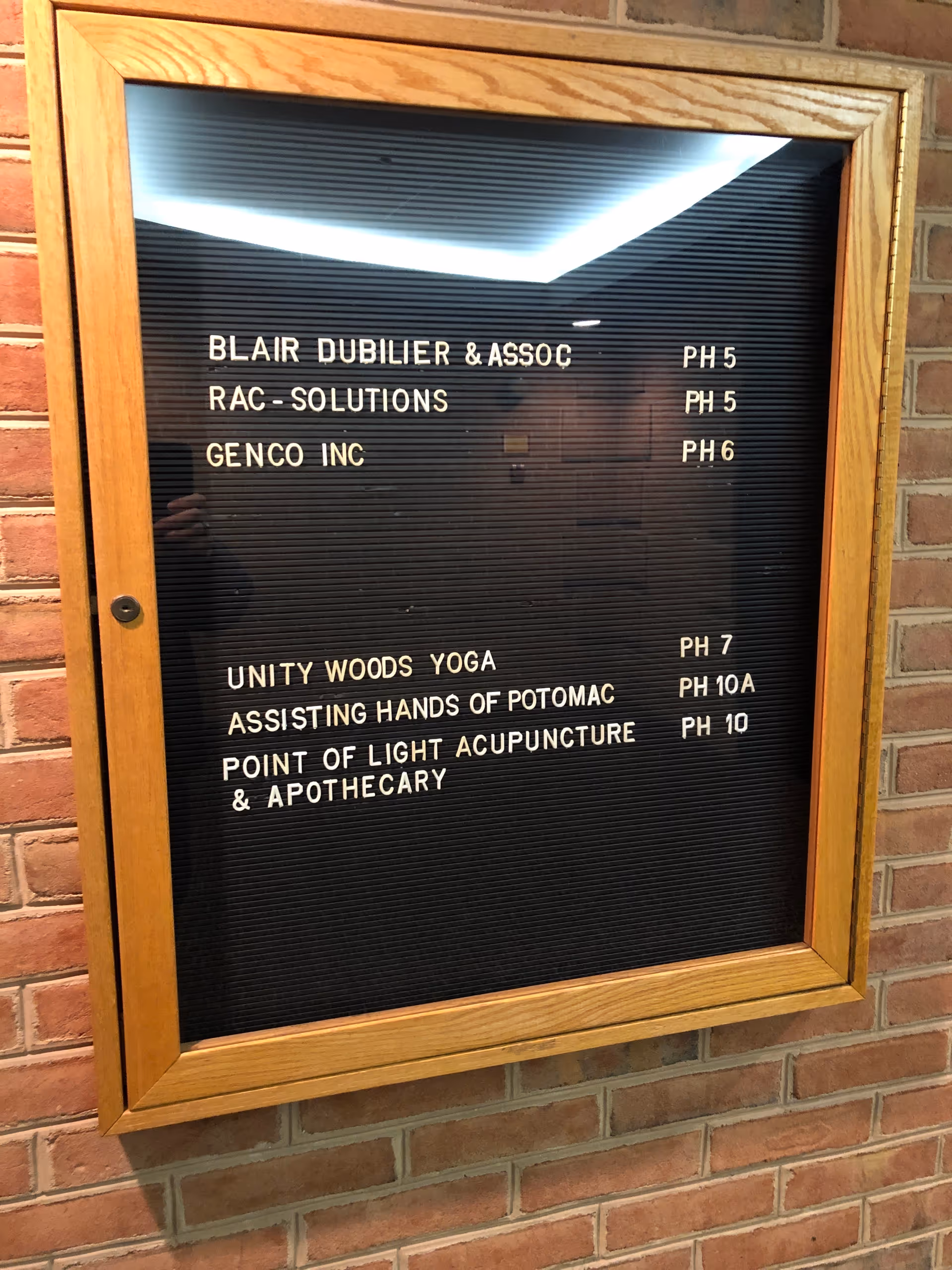 Wood-framed black directory board mounted on a brick wall listing offices.