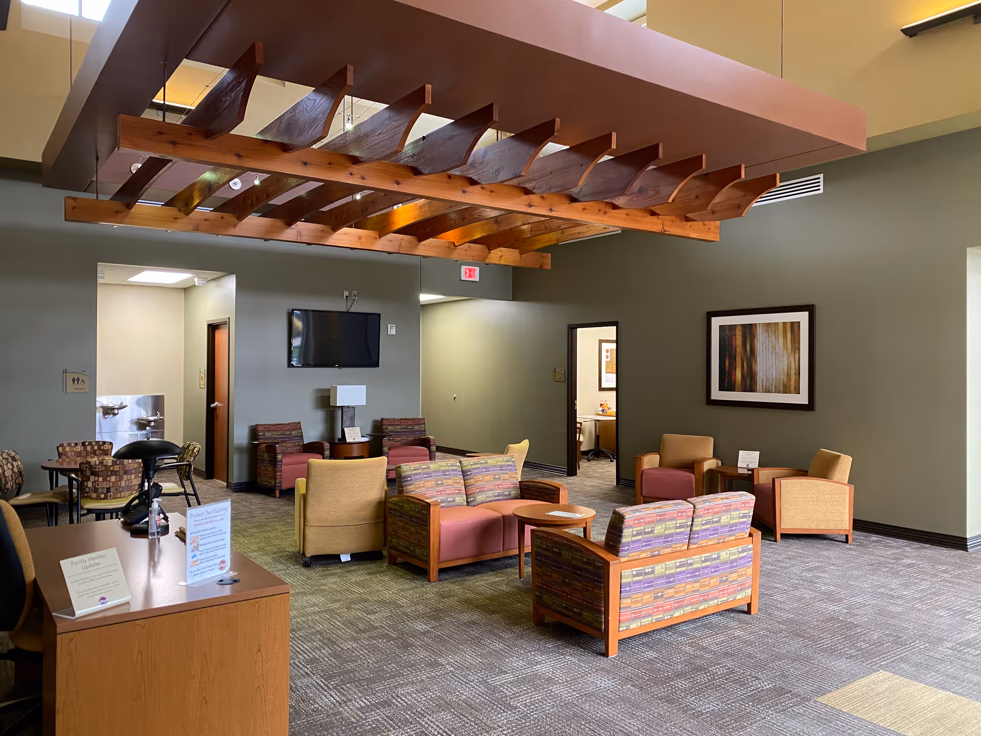 Senior facility lobby with colorful seating and a TV, featuring exposed wooden ceiling beams.