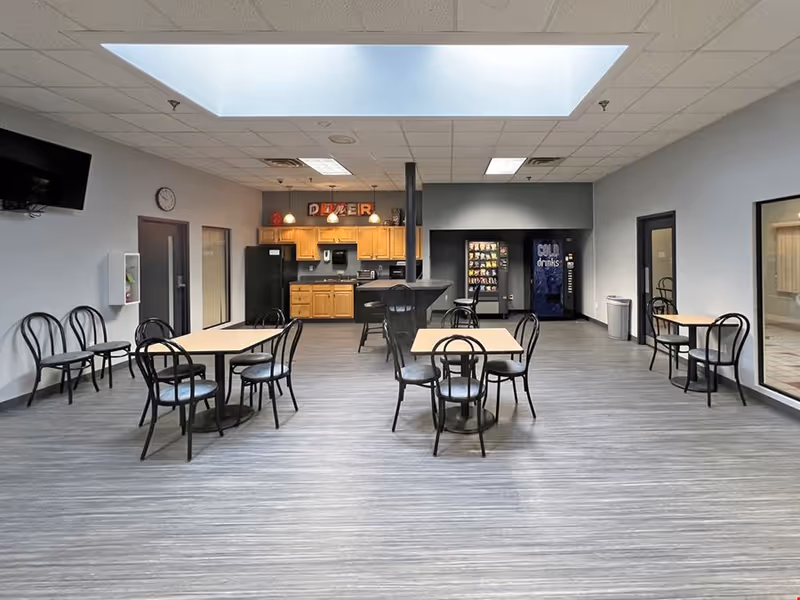 Interior dining area with multiple tables and chairs, kitchenette in back, vending machines.