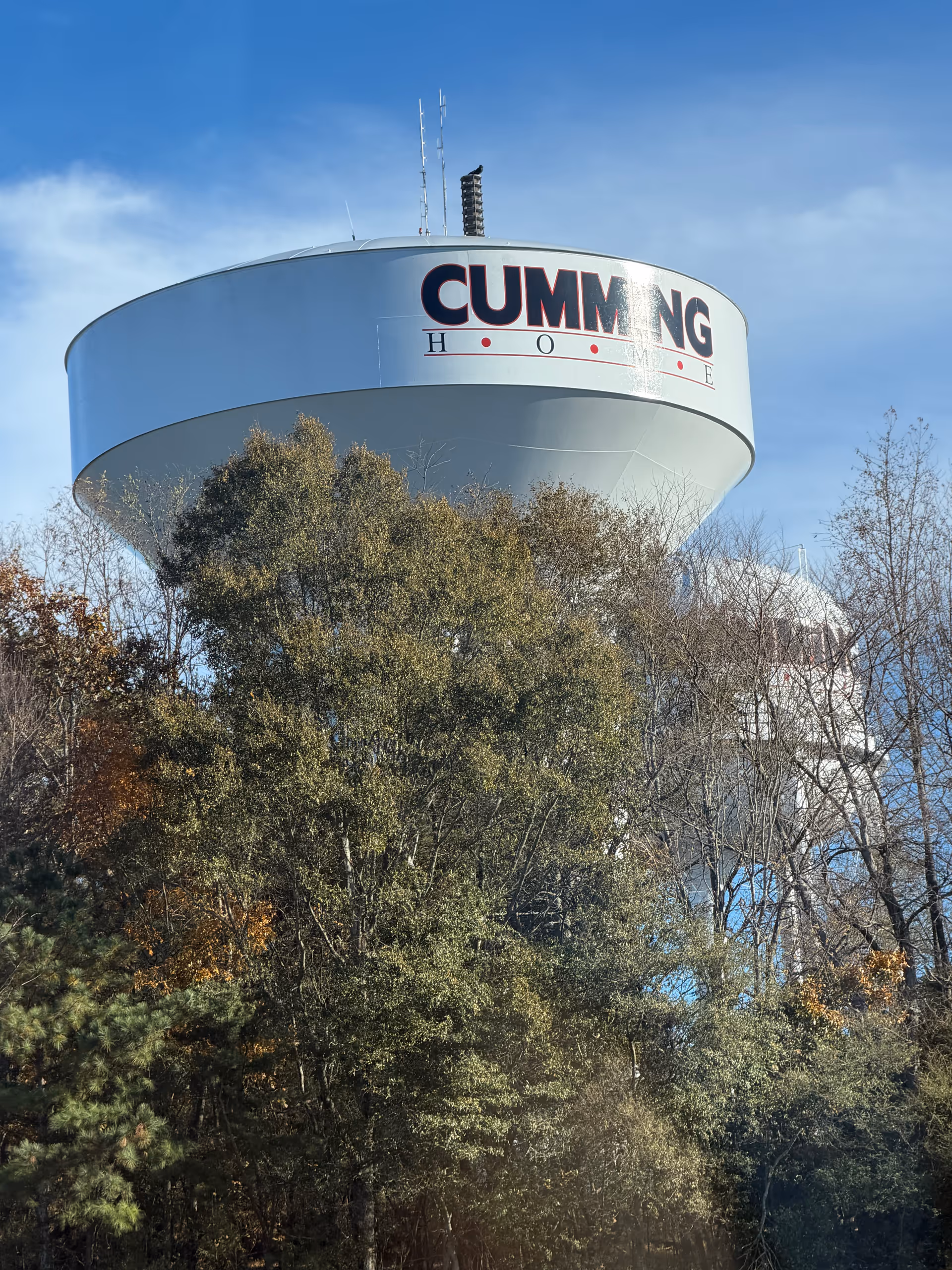 Large water tower labeled CUMMING rises above trees under a blue sky