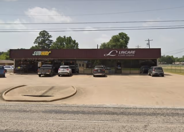 Exterior of a strip building with LINCARE and Subway storefronts and parked cars in front.