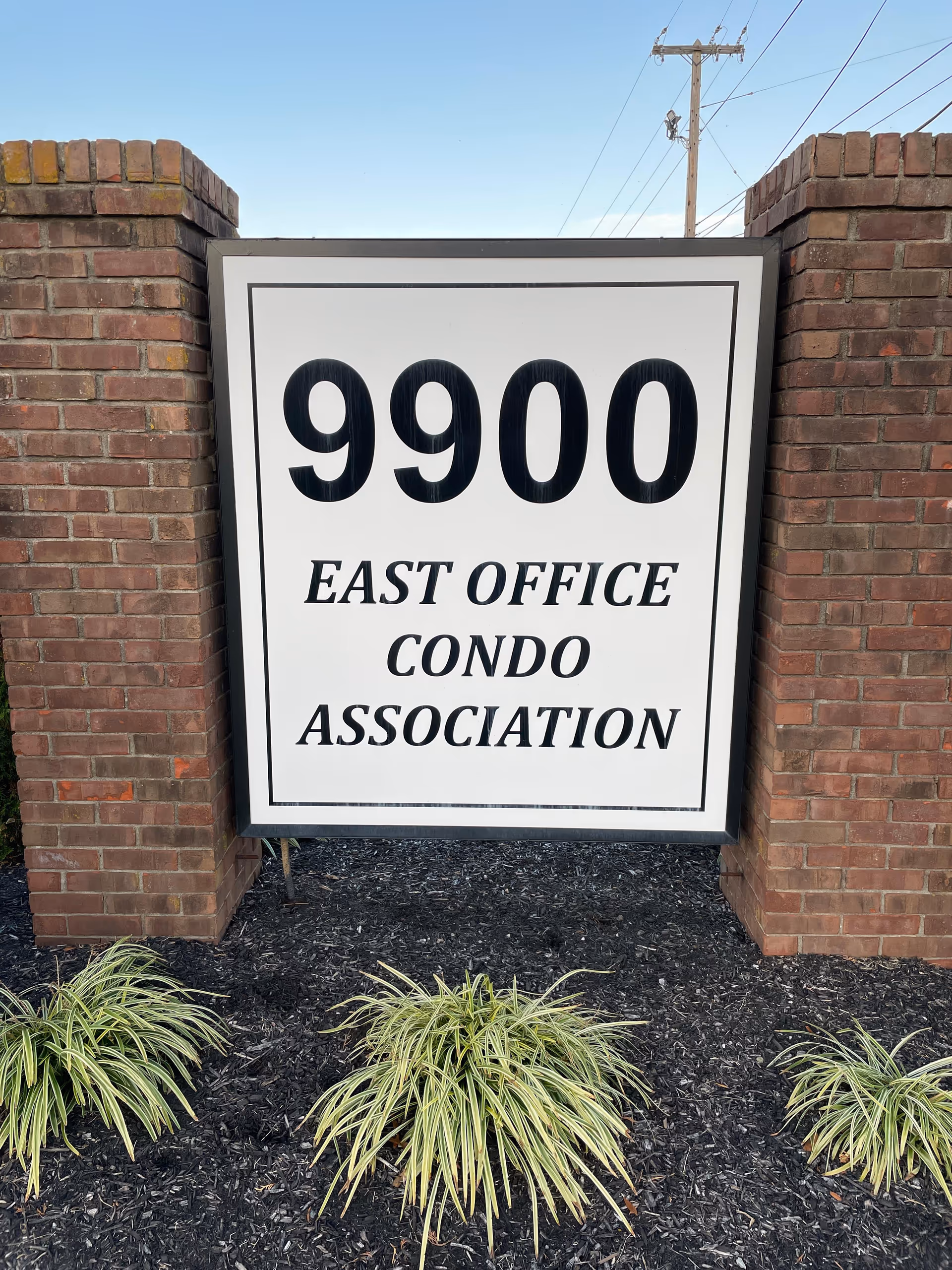 Large white sign reading 9900 East Office Condo Association between brick pillars.