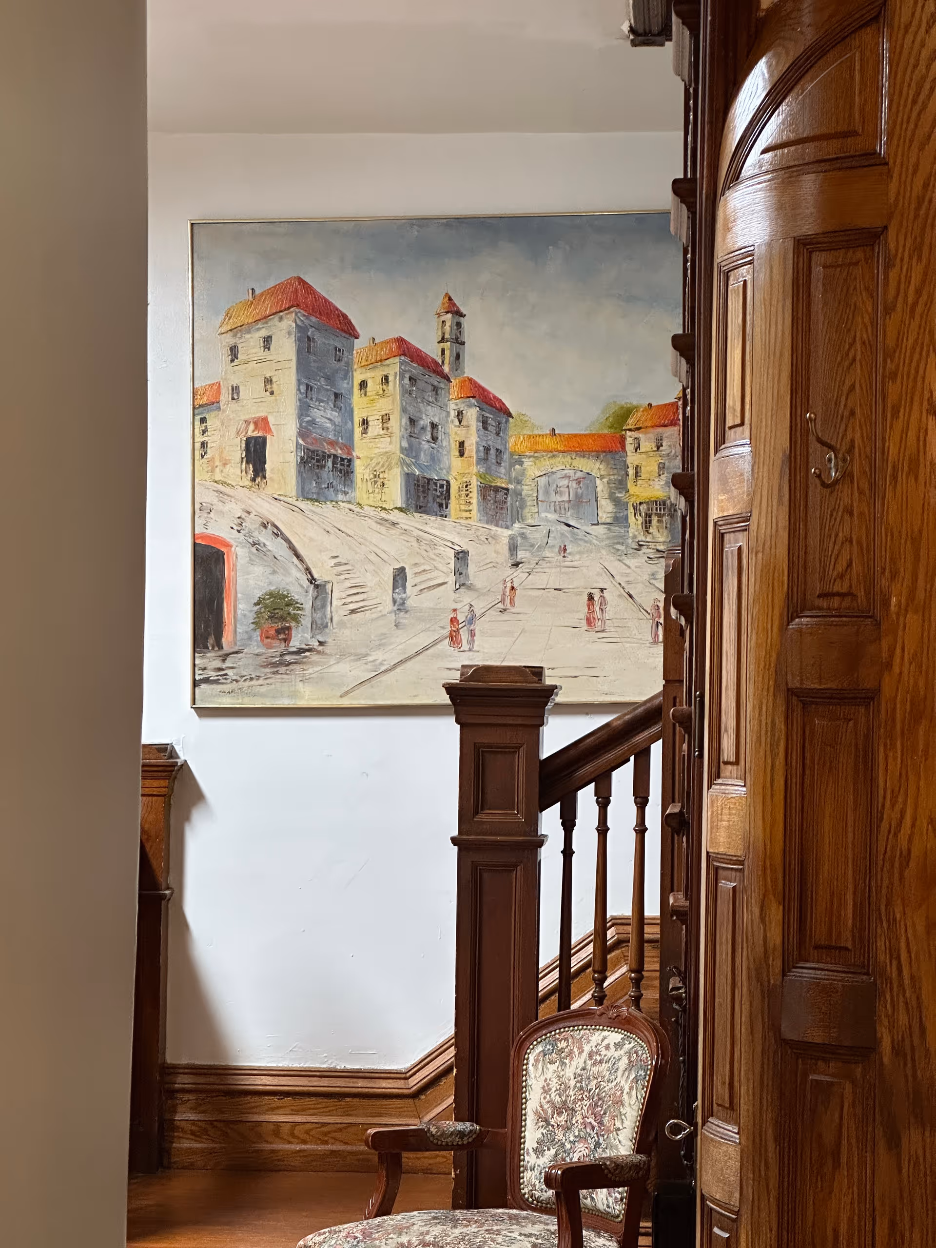 In a wood panel interior, a staircase and mural dominate the space beside an upholstered chair.