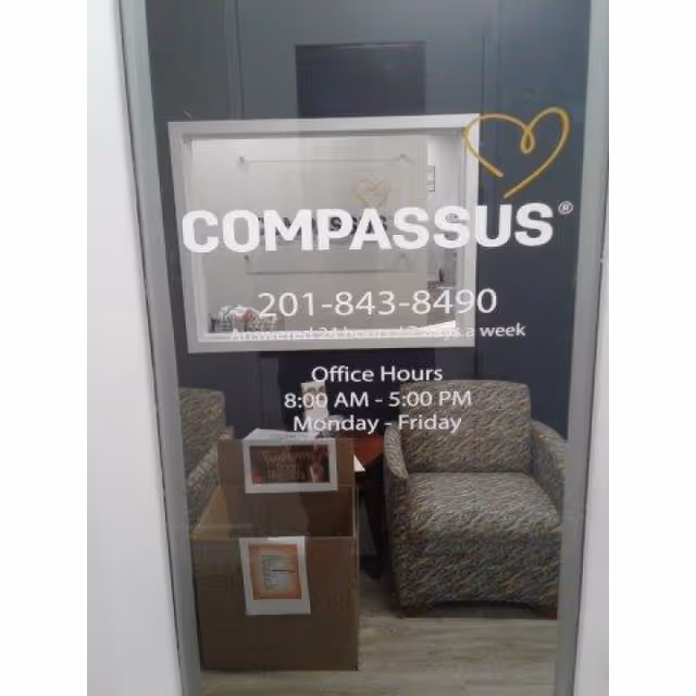 Interior doorway with Compassus logo, office chairs, and a cardboard box.