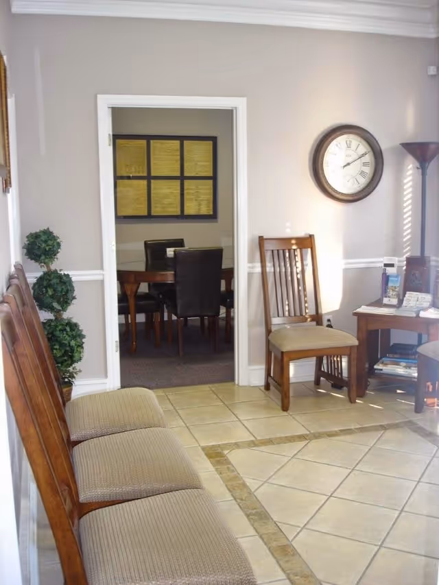 Lobby waiting area with wooden chairs, doorway to a meeting room, wall clock, and brochures.