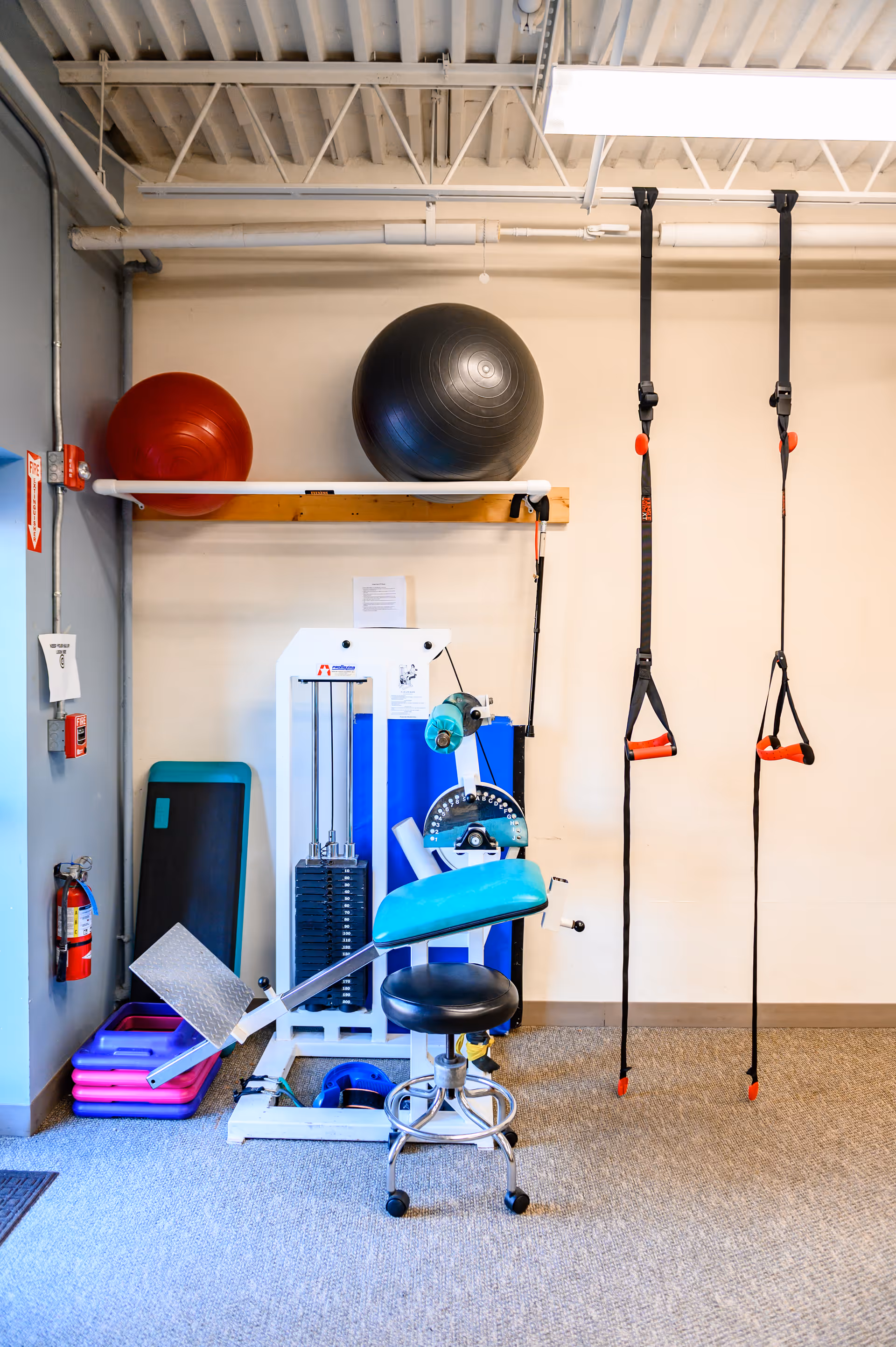 Interior physical therapy gym featuring exercise machines, stability balls, straps, and a padded chair.