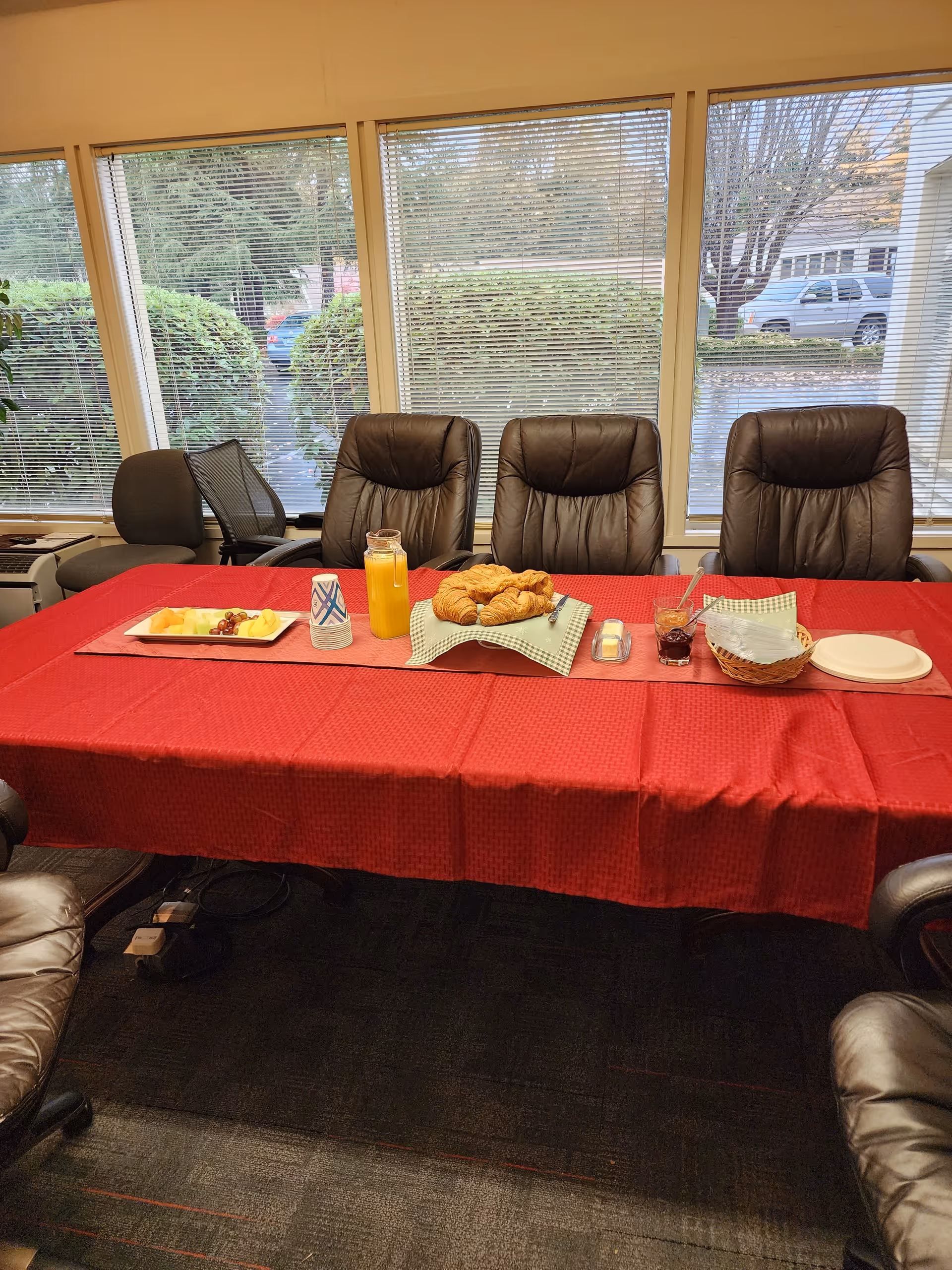 Inside dining area with a long red table, pastries, juice, and leather chairs.