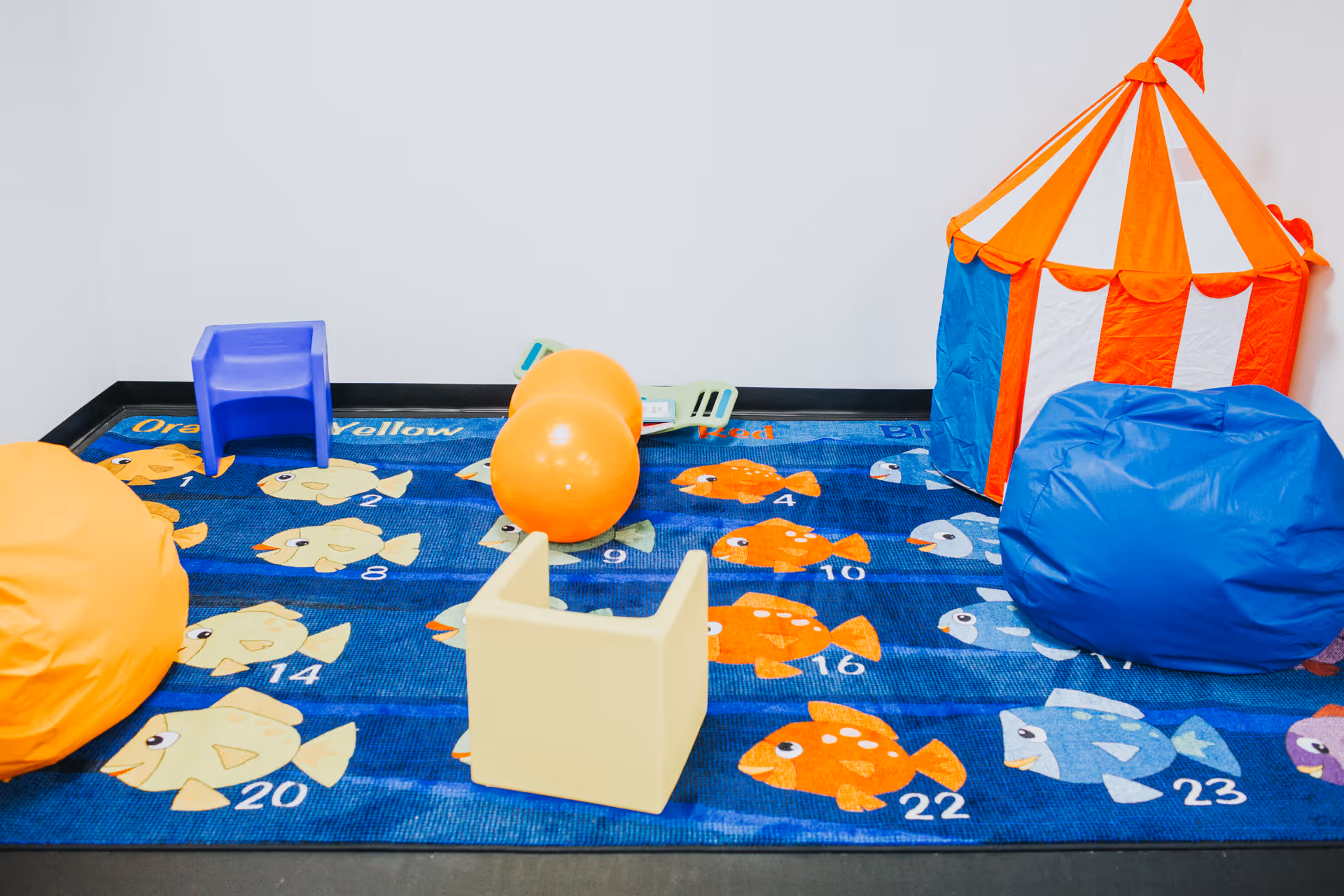 Colorful indoor play area with fish-pattern carpet, toys, tent, and beanbags.