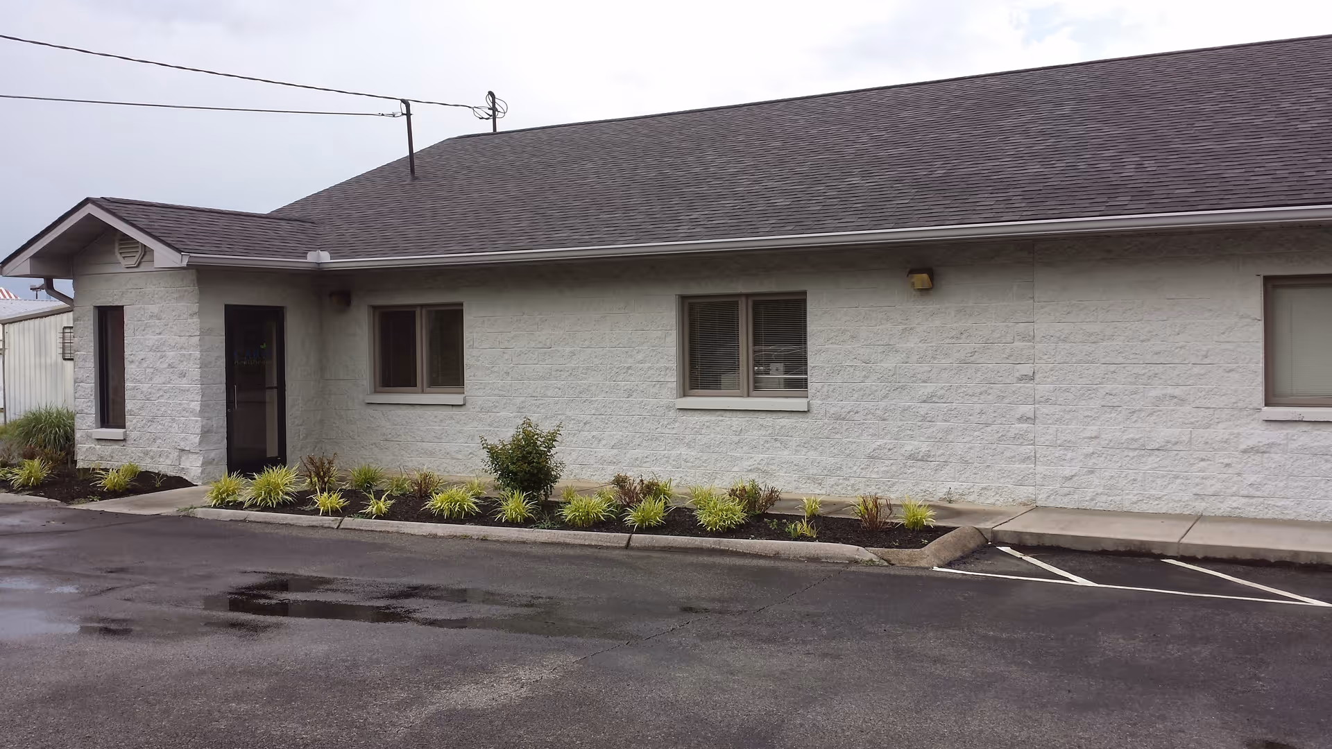 Single-story senior living facility exterior with entry door, windows, and landscaped front shrubs.