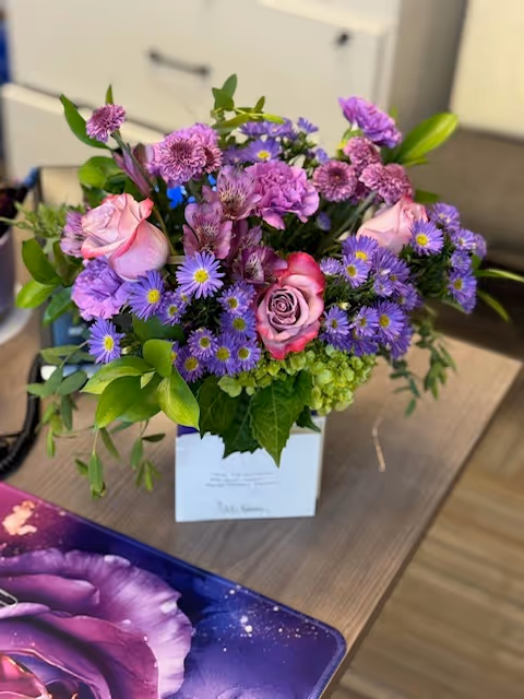 Bouquet of pink and purple flowers in a vase on a wooden desk in an office.