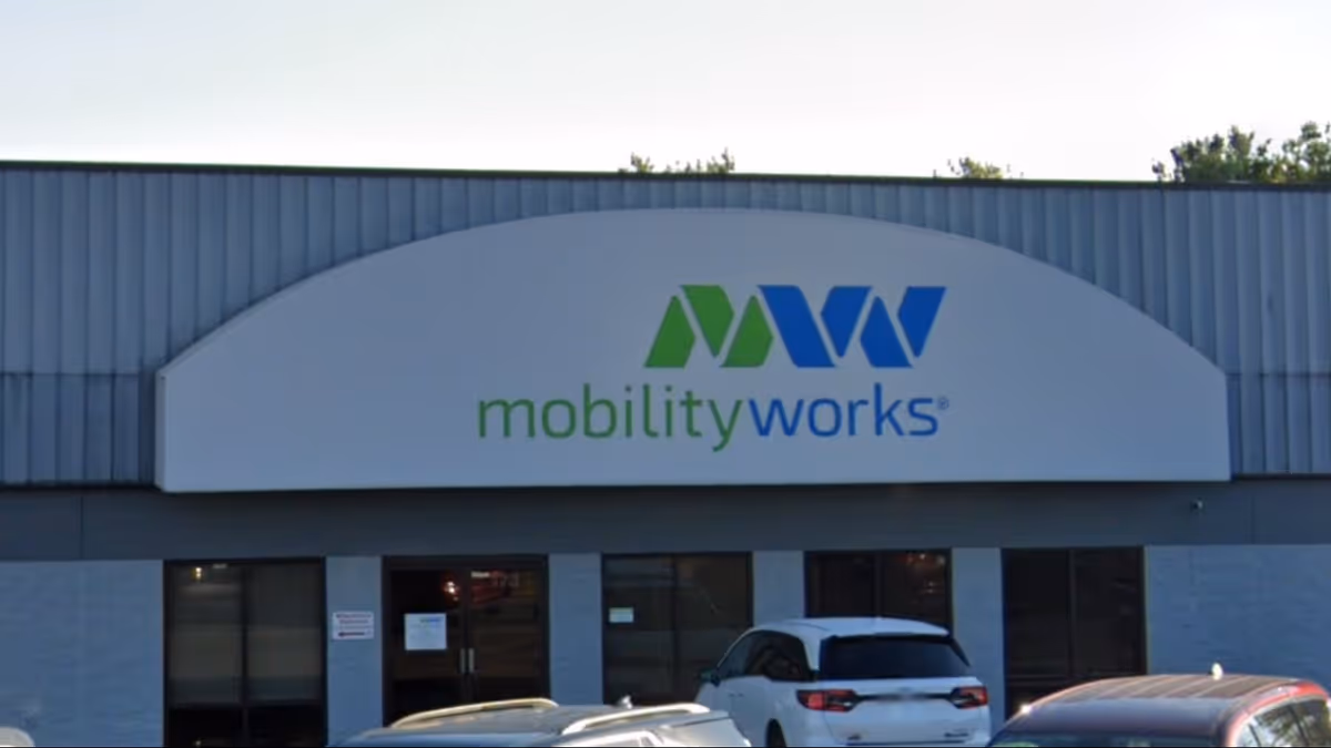 Front view of a MobilityWorks facility with a curved sign and parked cars.