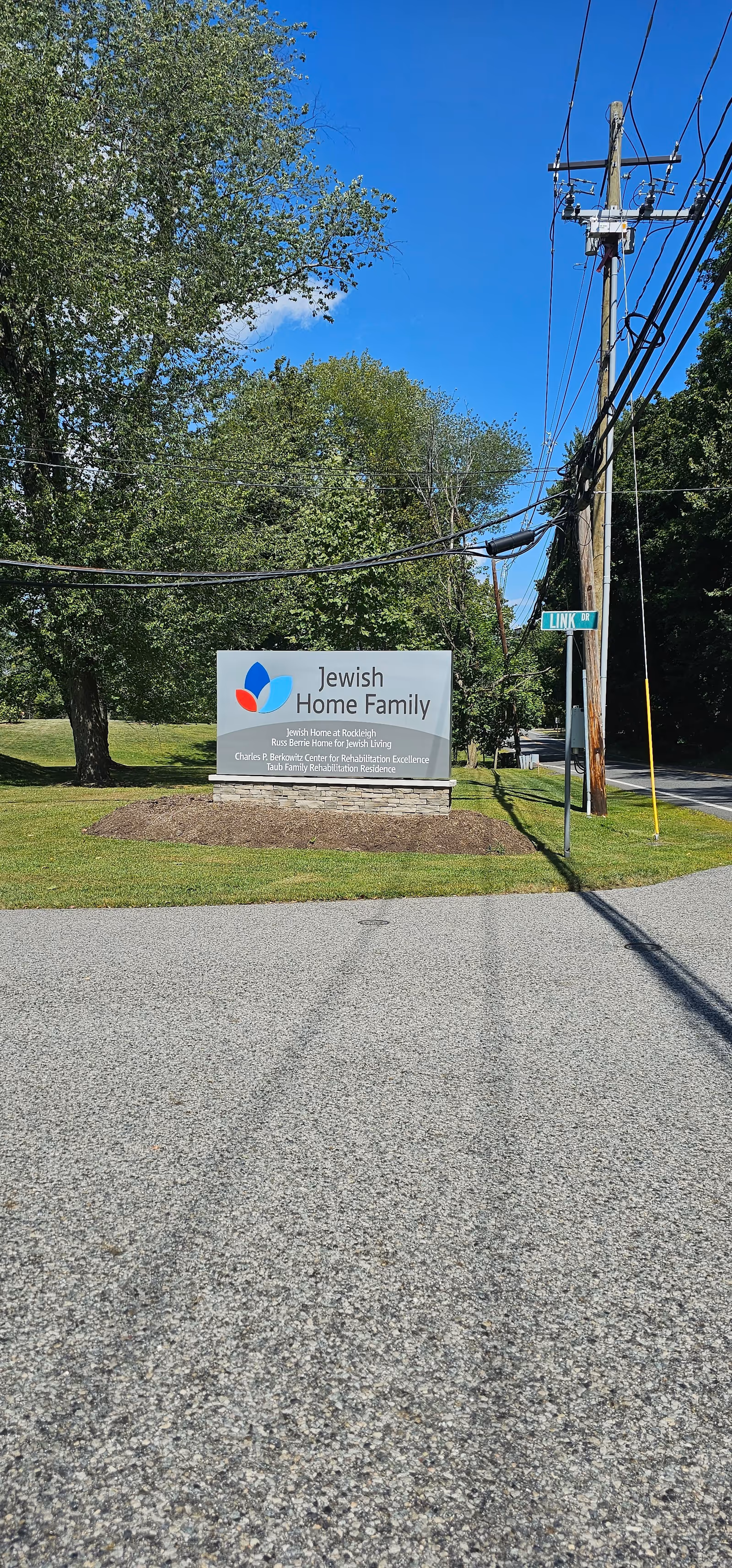 Jewish Home Family sign on a grassy roadside with trees and power lines.