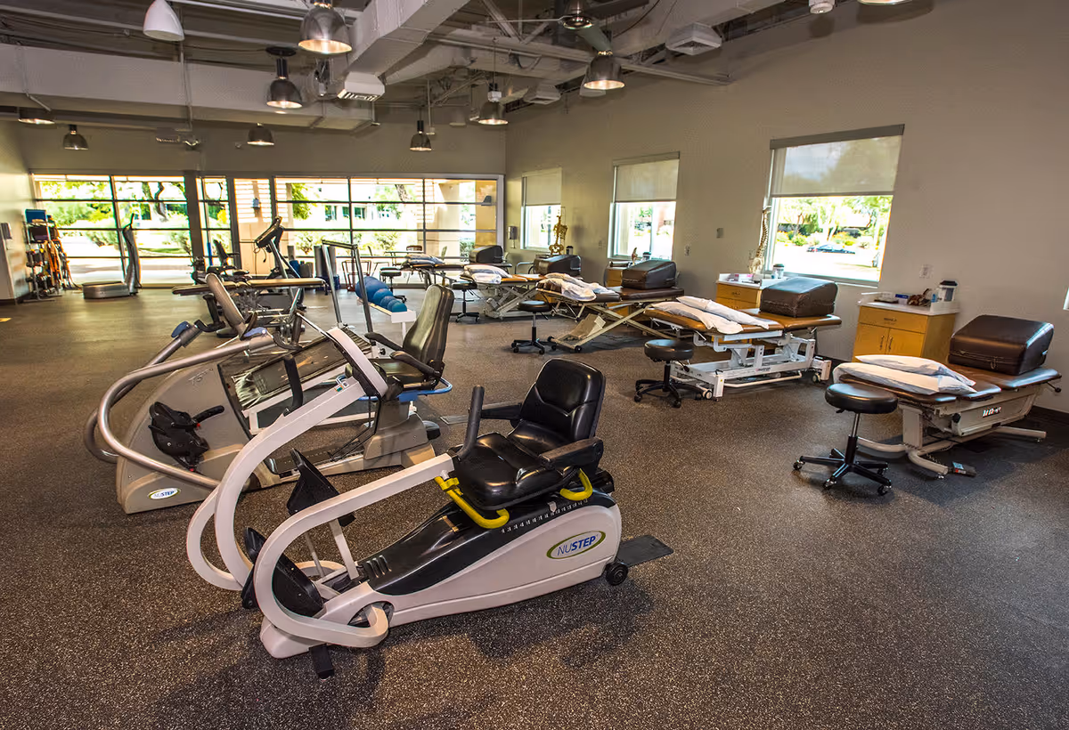 Bright therapy gym with treadmills, exercise machines, and treatment tables in a spacious room.