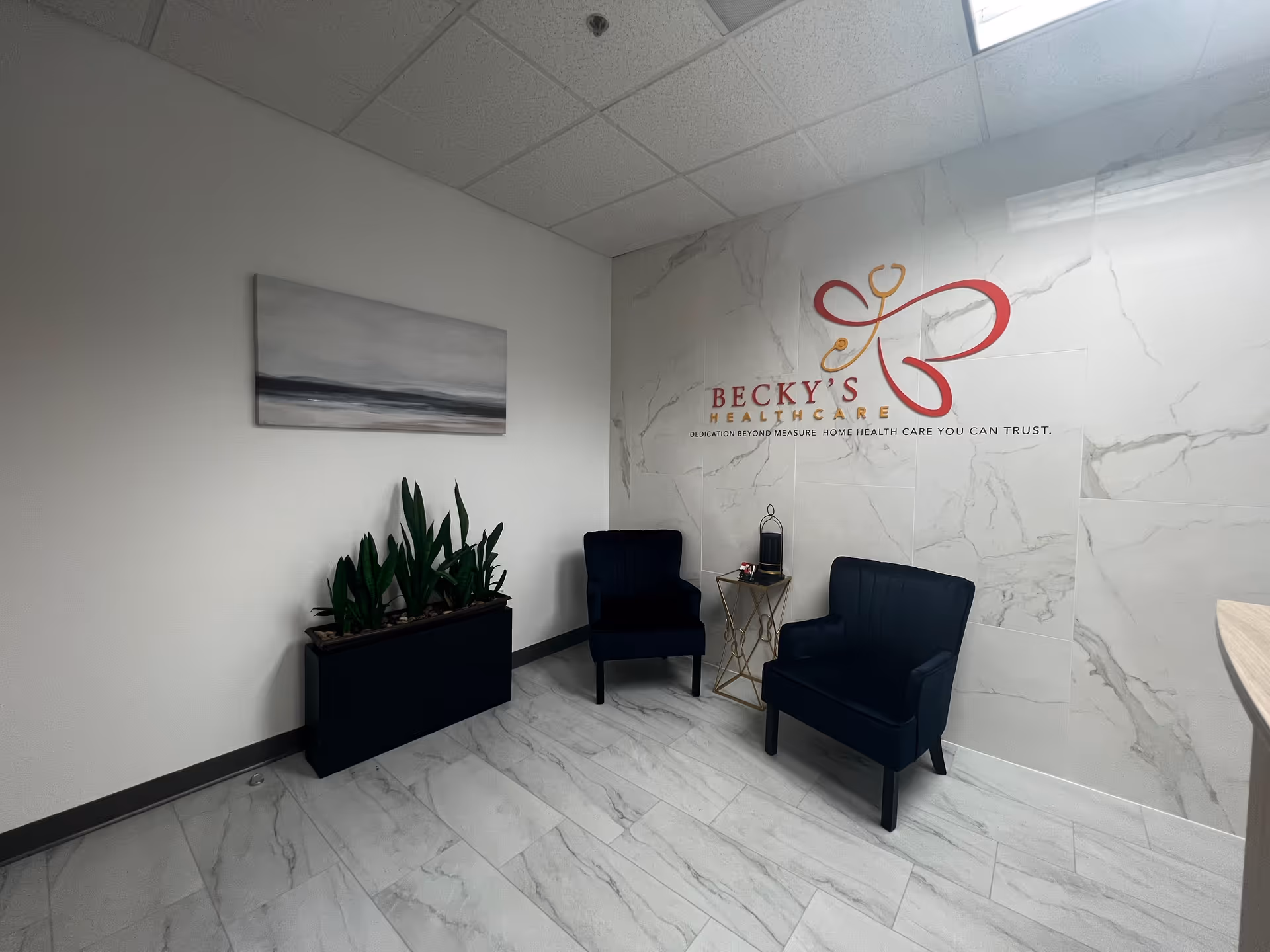 Lobby area with two navy chairs, planter, and Becky's HealthCare logo on marble wall