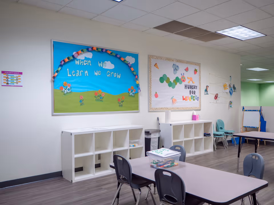 Bright classroom/therapy room with tables, chairs, cubbies, and colorful posters on the walls.