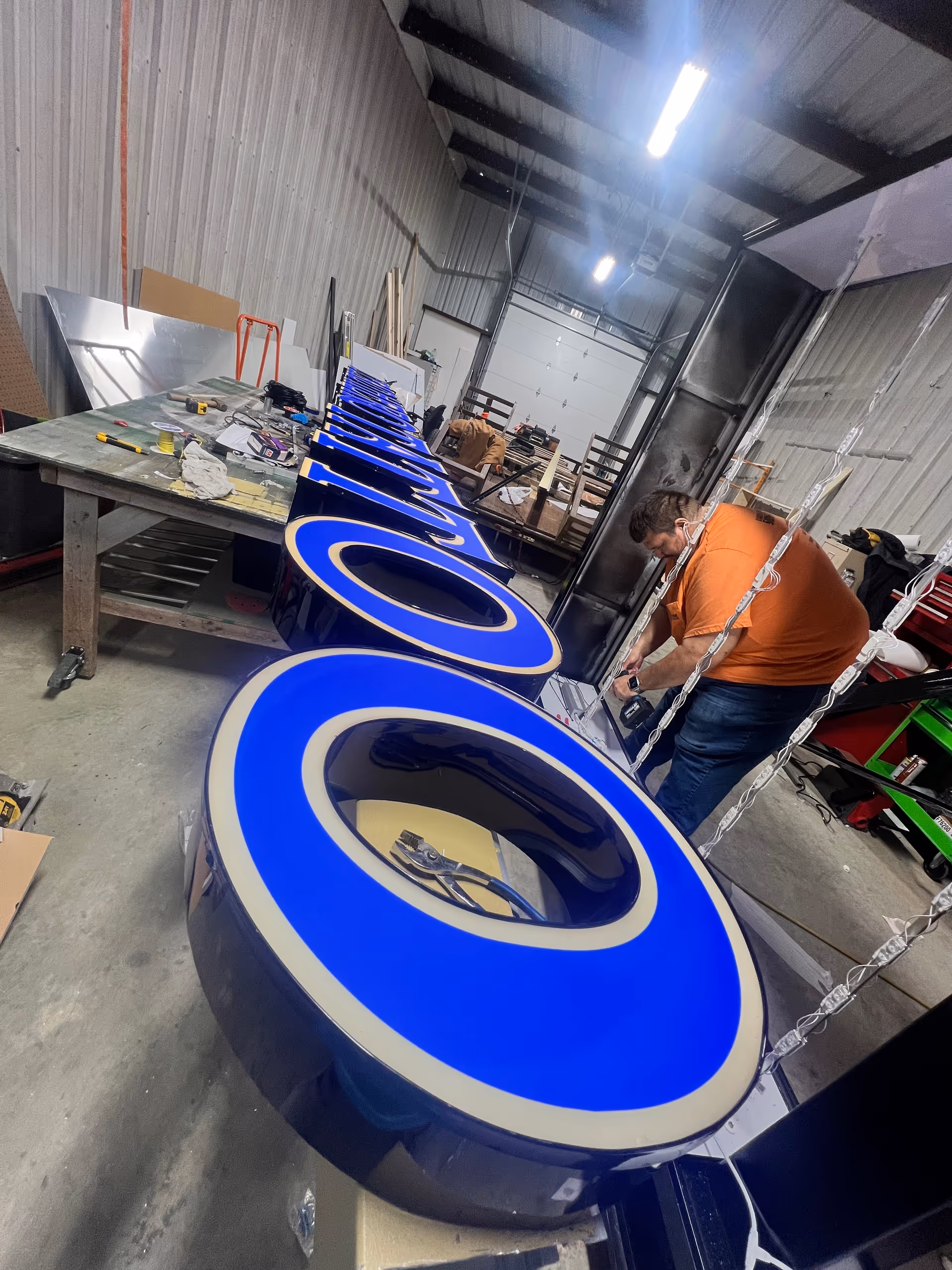 Interior workshop with large blue illuminated sign letters on a workbench and a worker