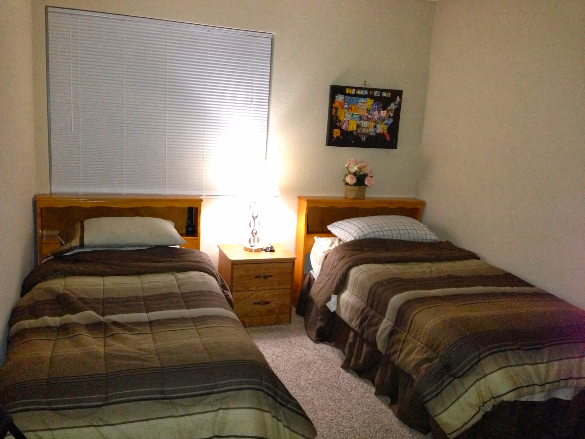 Two twin beds with a nightstand and lamp in a small, shared bedroom.