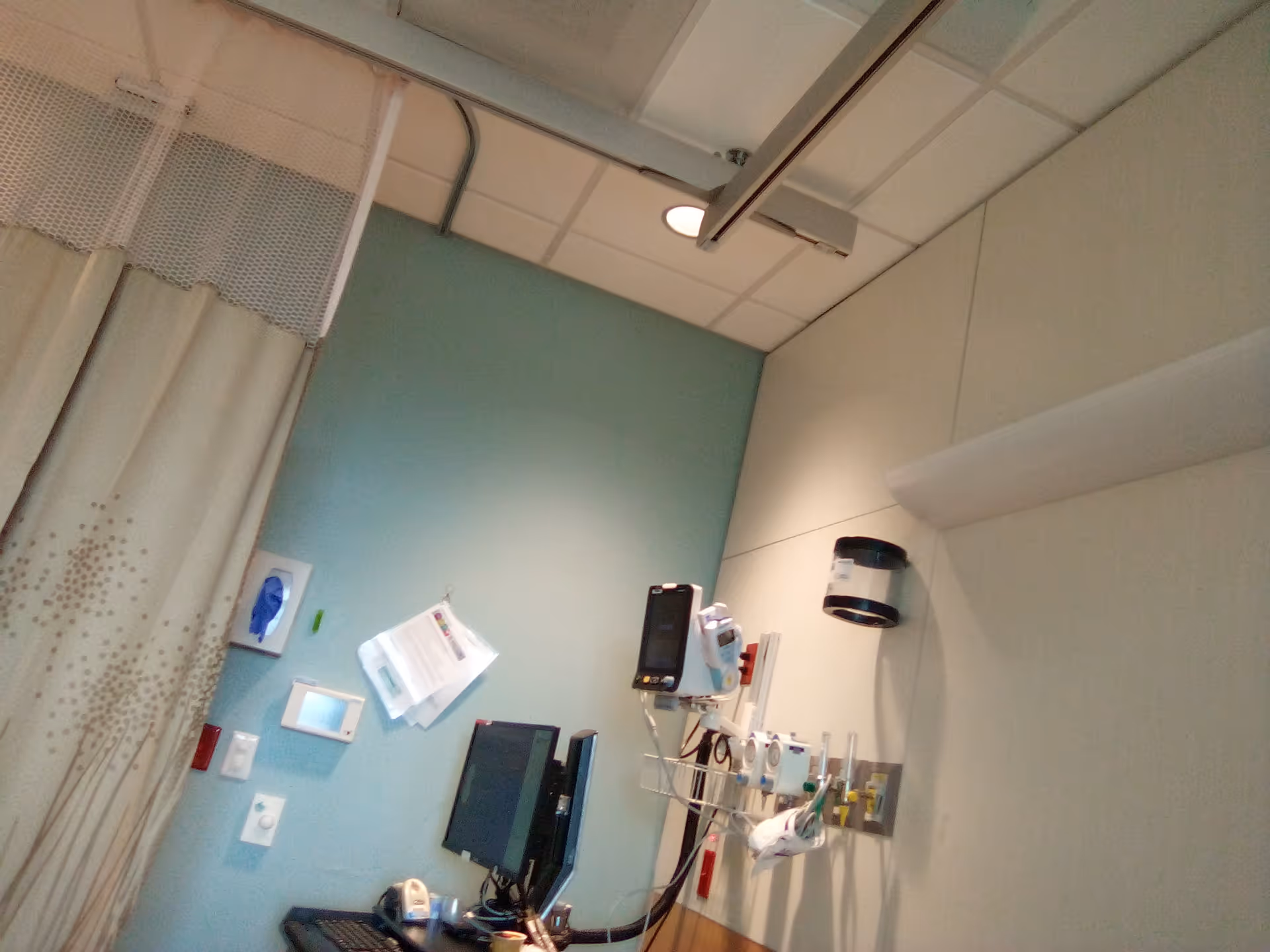 Hospital patient room corner with monitoring equipment, IV pole, and privacy curtain.