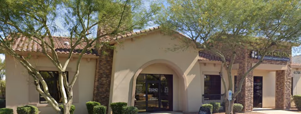Front exterior of a Senior Helpers facility with arched entrance and surrounding trees.