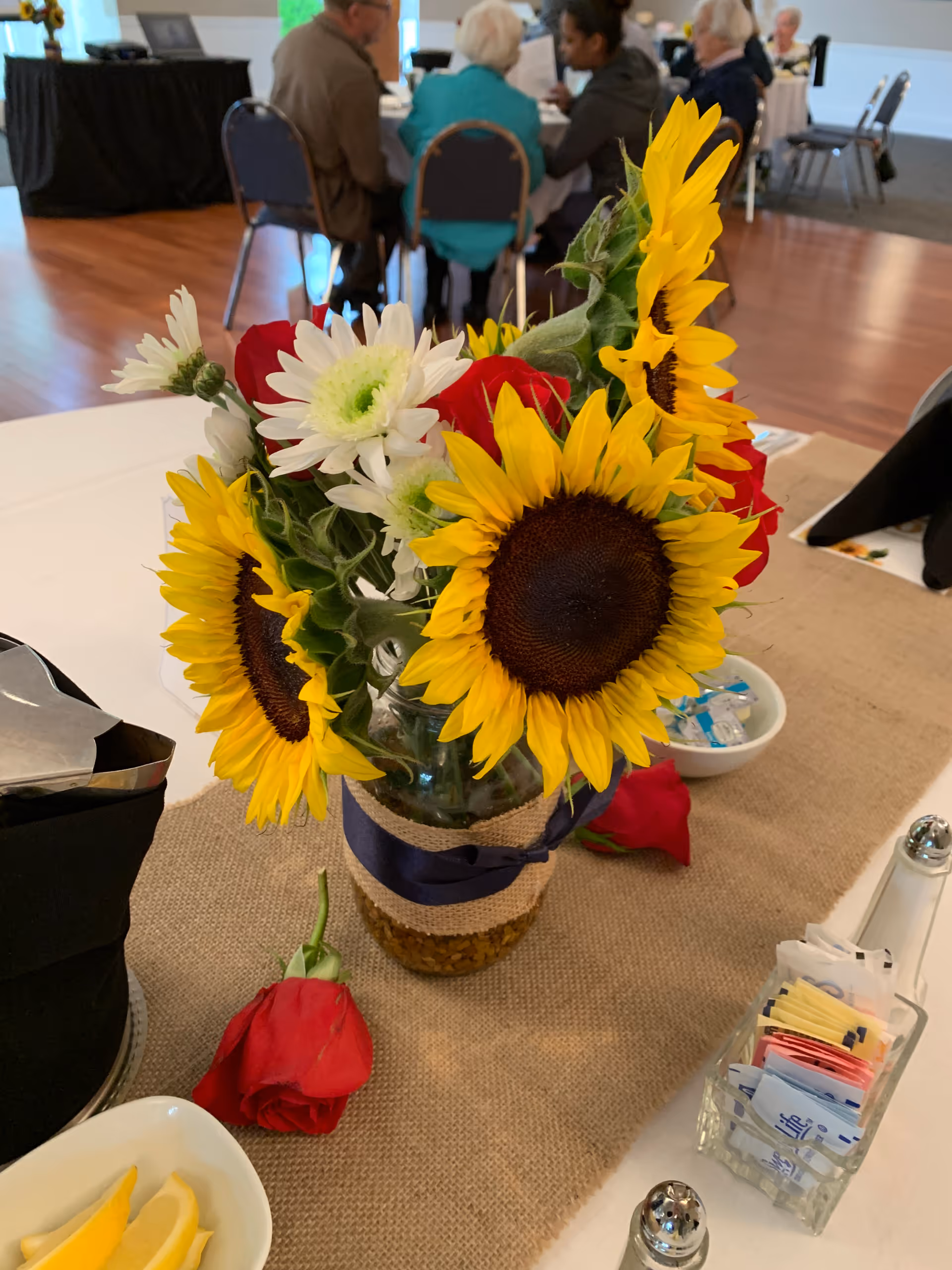 Sunflower centerpiece on a dining table with seniors dining in the background.
