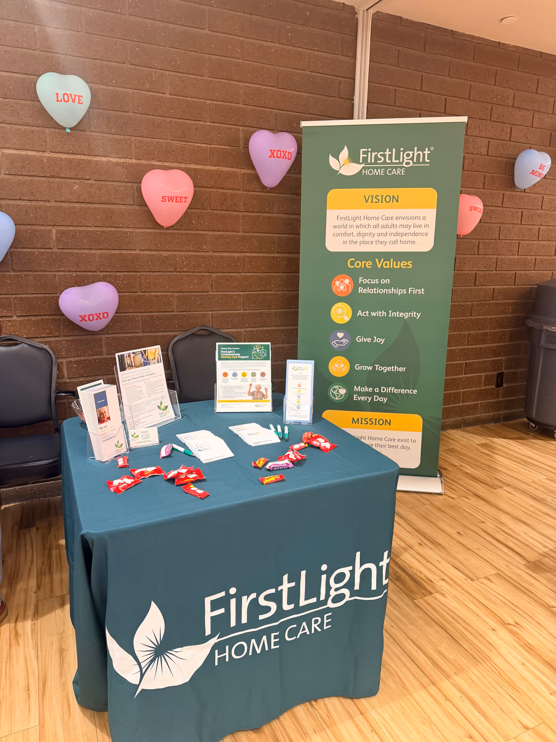 Indoor lobby area with FirstLight Home Care table, banner, and heart-shaped balloons.