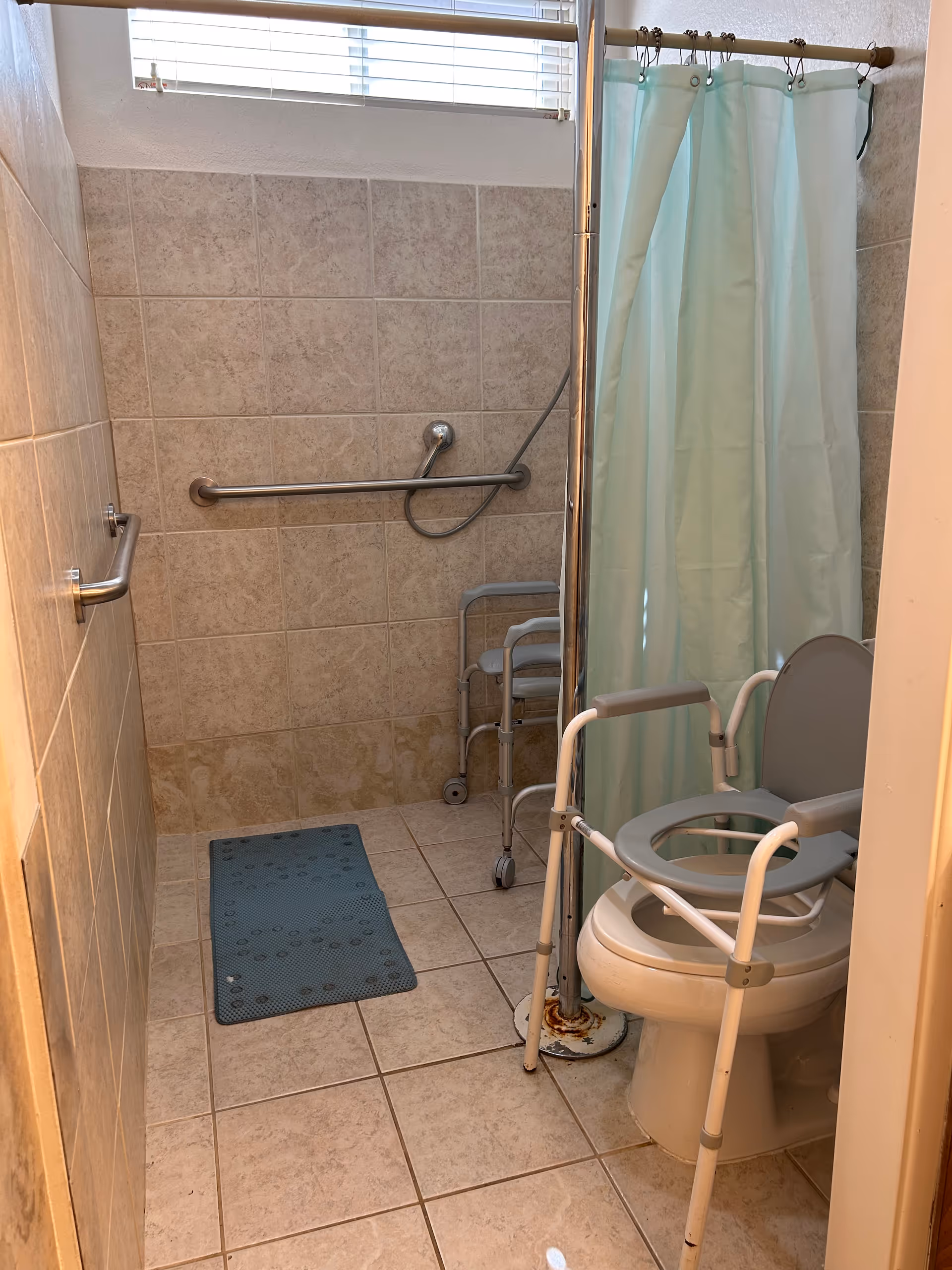 Accessible bathroom with grab bars, shower curtain, walker, and toilet.