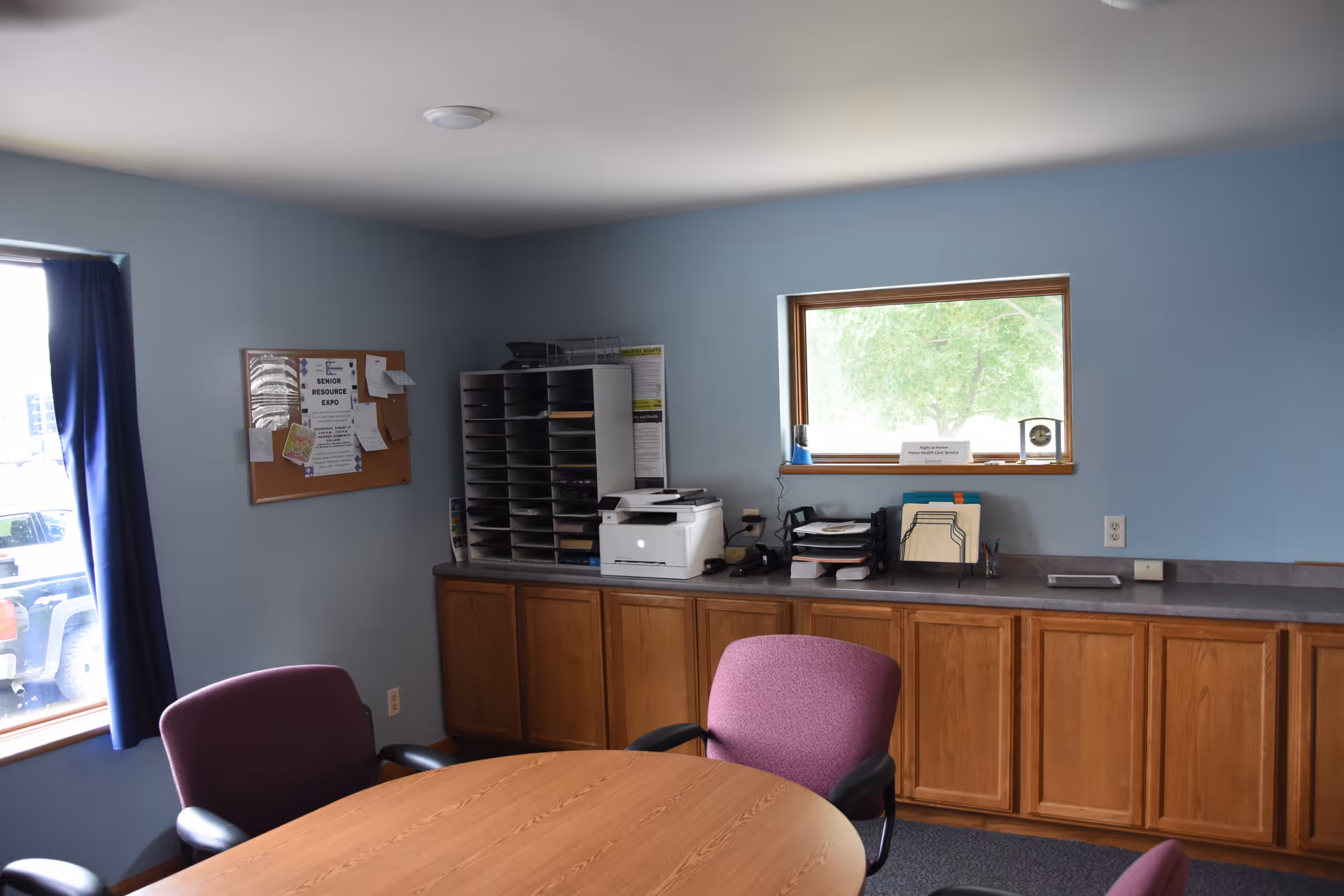 A small office in a senior living facility with cabinets, printer, and a round table.