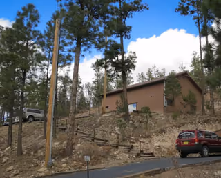 Exterior view of a brown hospice building on a hillside with tall pine trees.
