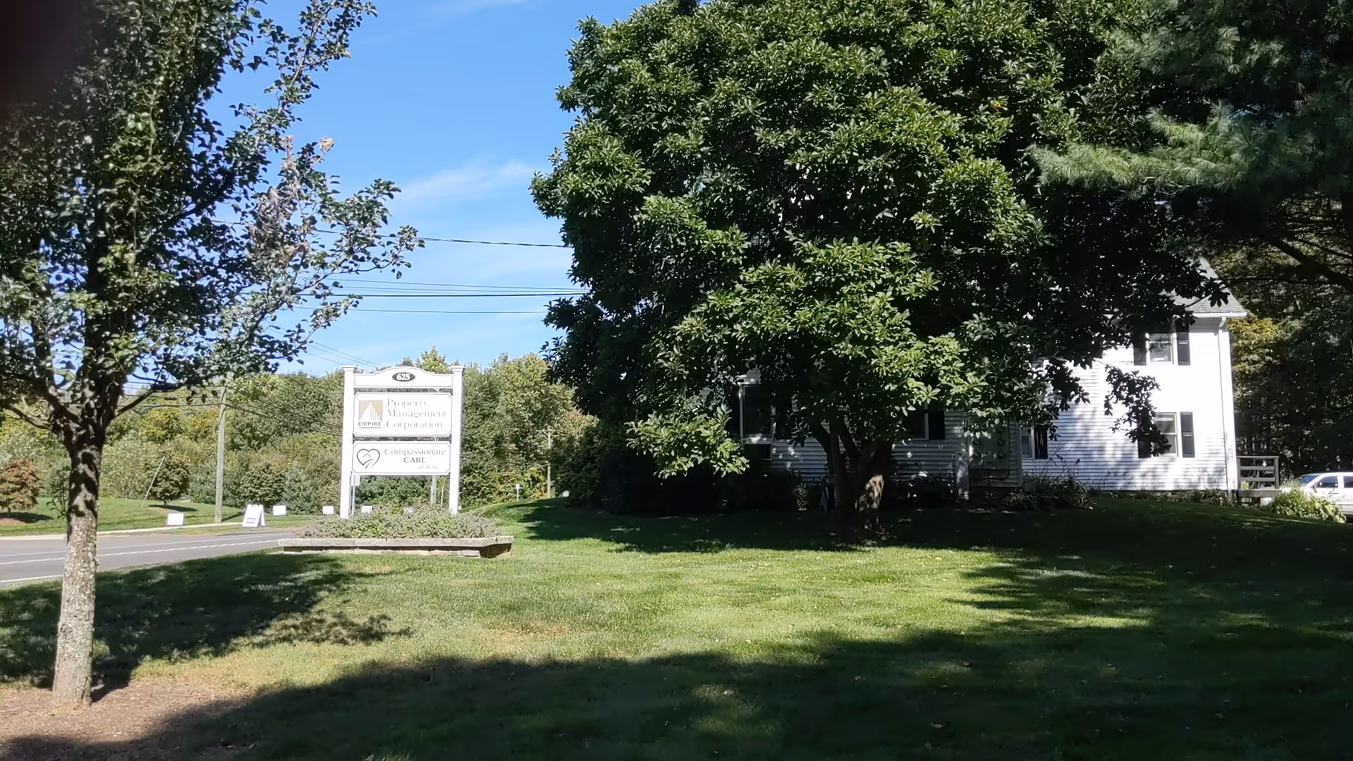White two-story building surrounded by trees with a large sign on the lawn.