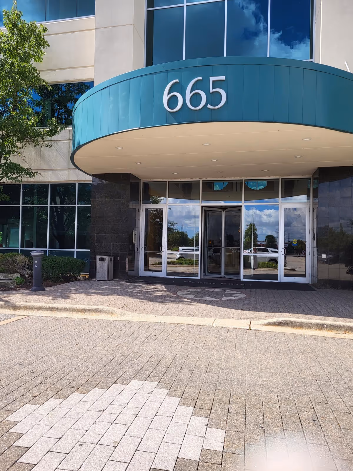 Modern building entrance with teal curved canopy and glass doors marked 665.