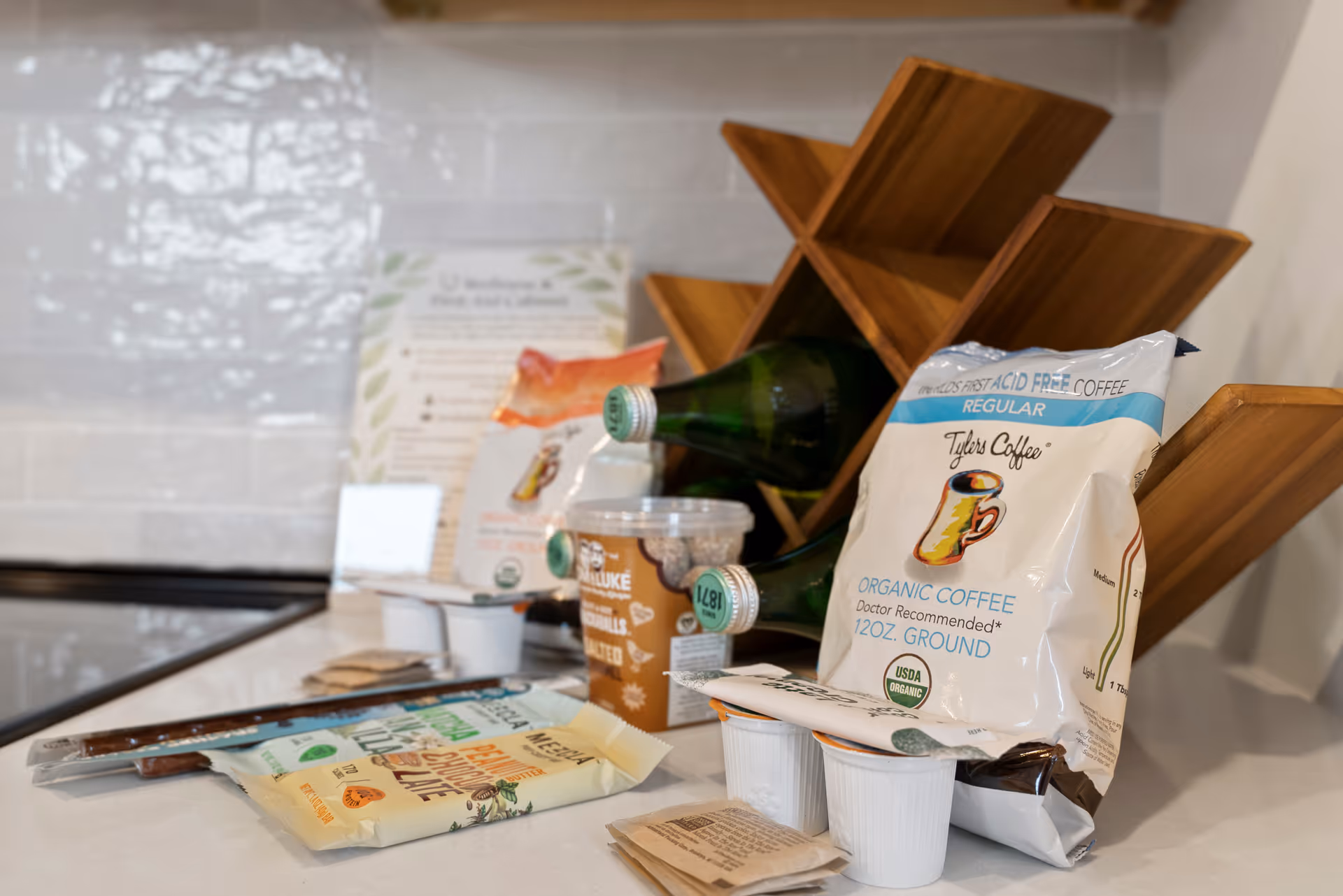 Countertop with coffee packets, cups, and a wooden shelf in a bright kitchen.