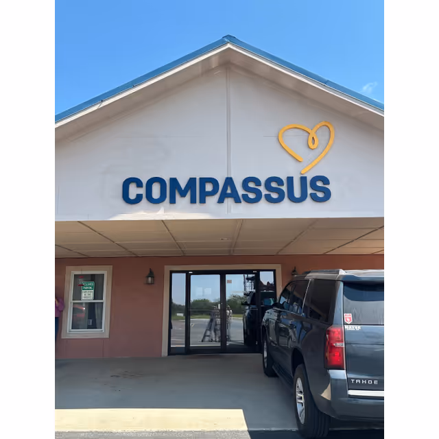 Front view of Compassus senior living facility with entrance doors and a parked SUV.