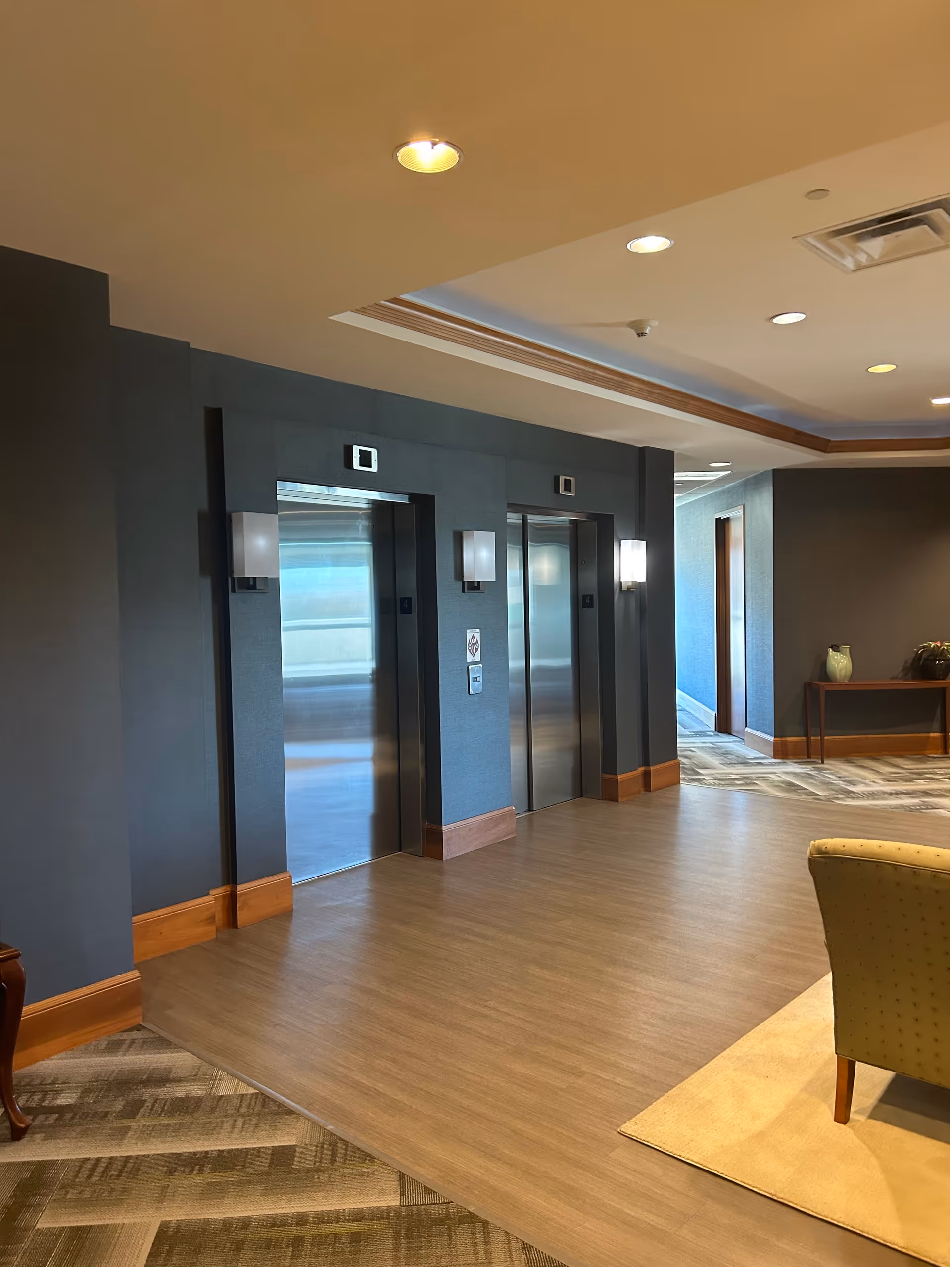 Interior hallway with two elevator doors, dark blue walls, and wooden baseboards
