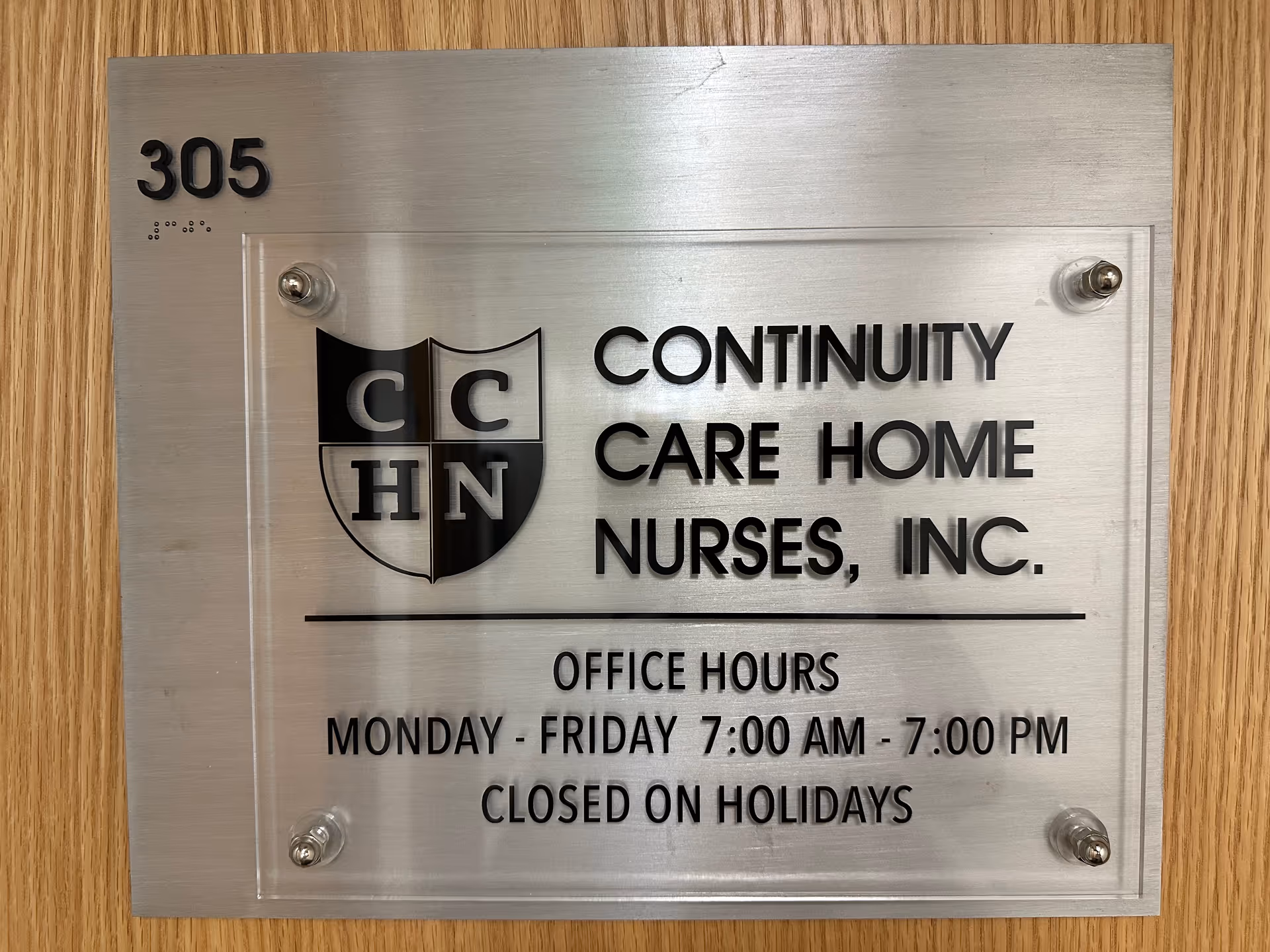 Metal plaque on a wooden wall showing Continuity Care Home Nurses, Inc., with office hours.