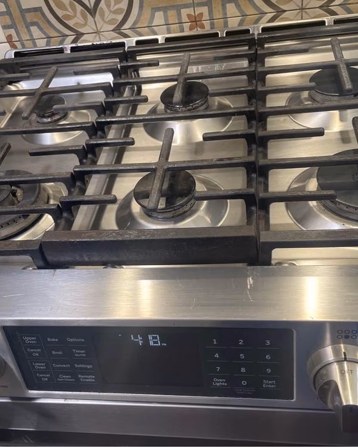 Stainless steel gas stove with multiple burners and digital controls in a kitchen.