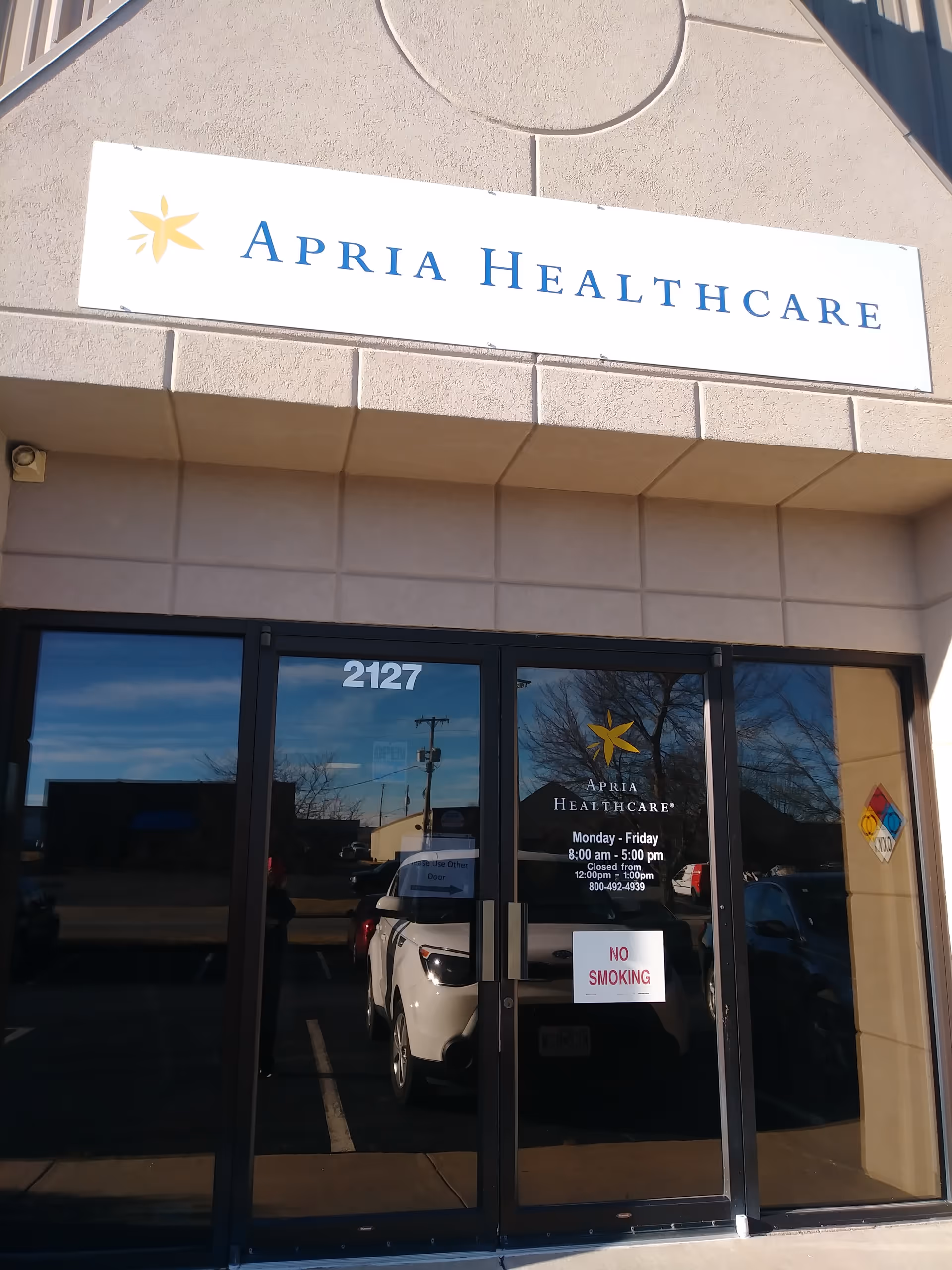 Front exterior of an Apria Healthcare facility with a glass entrance and sign