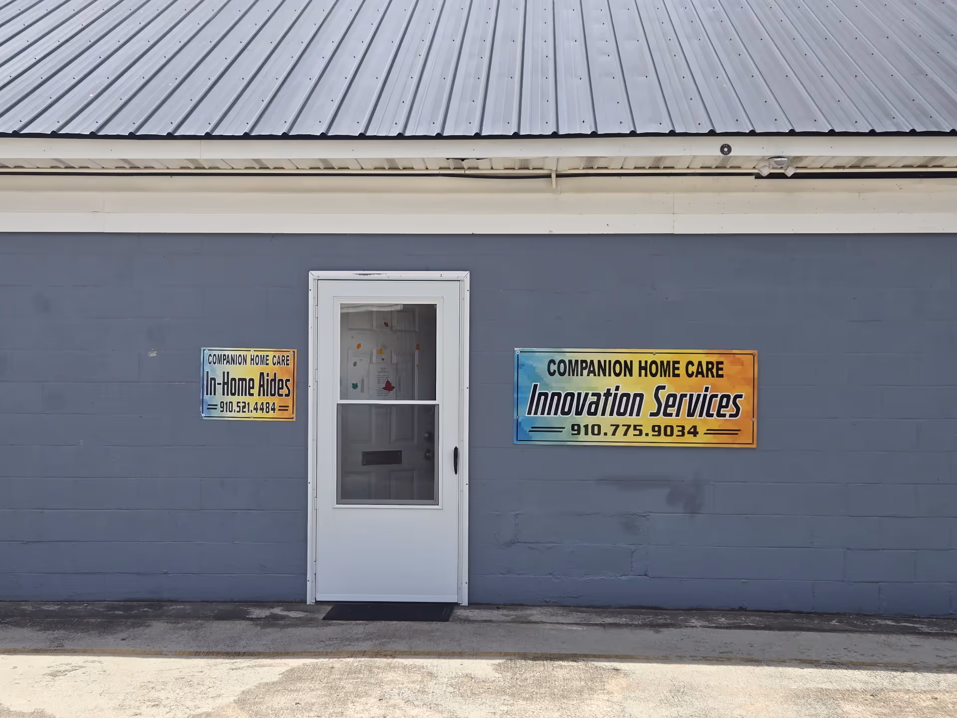 Grey exterior wall with a white door and two colorful Companion Home Care signs.