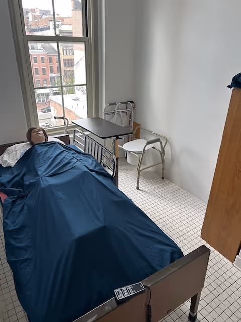 A bed in a small room with a blue sheet covering someone.