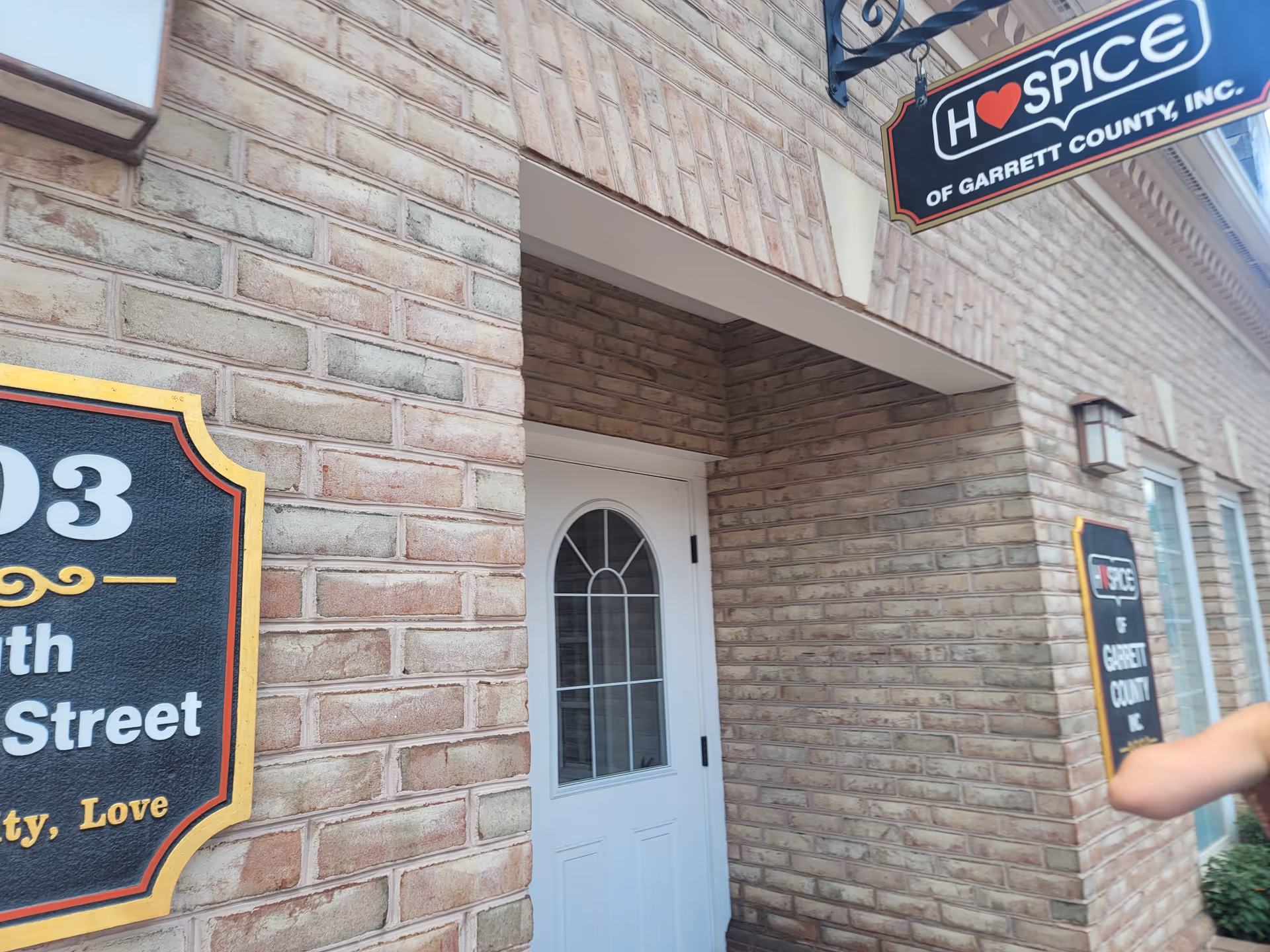 Brick building exterior with a white front door and Hospice of Garrett County sign.