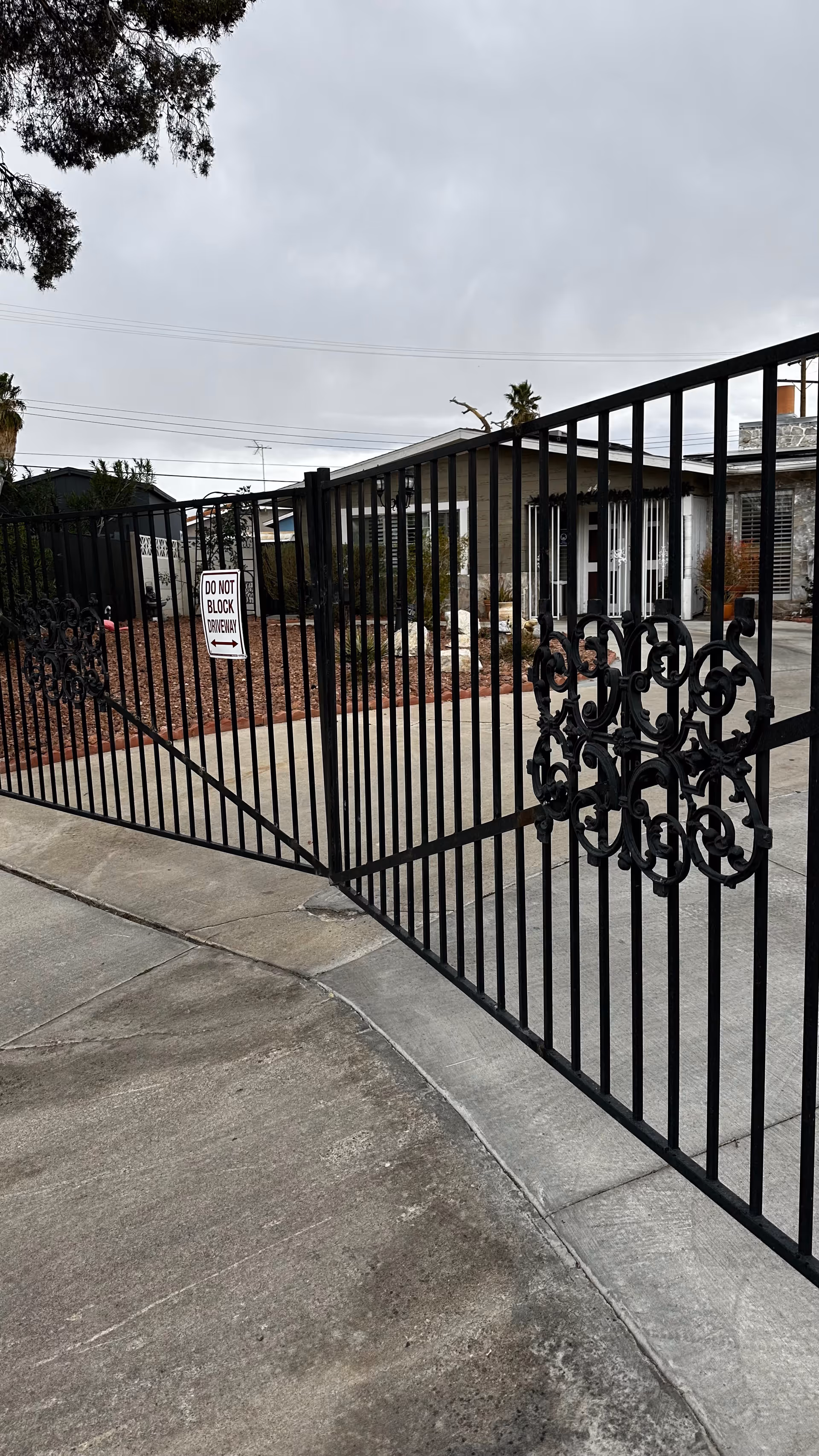 Wrought-iron gate opens to the exterior of a care home, with a driveway and shrubs.
