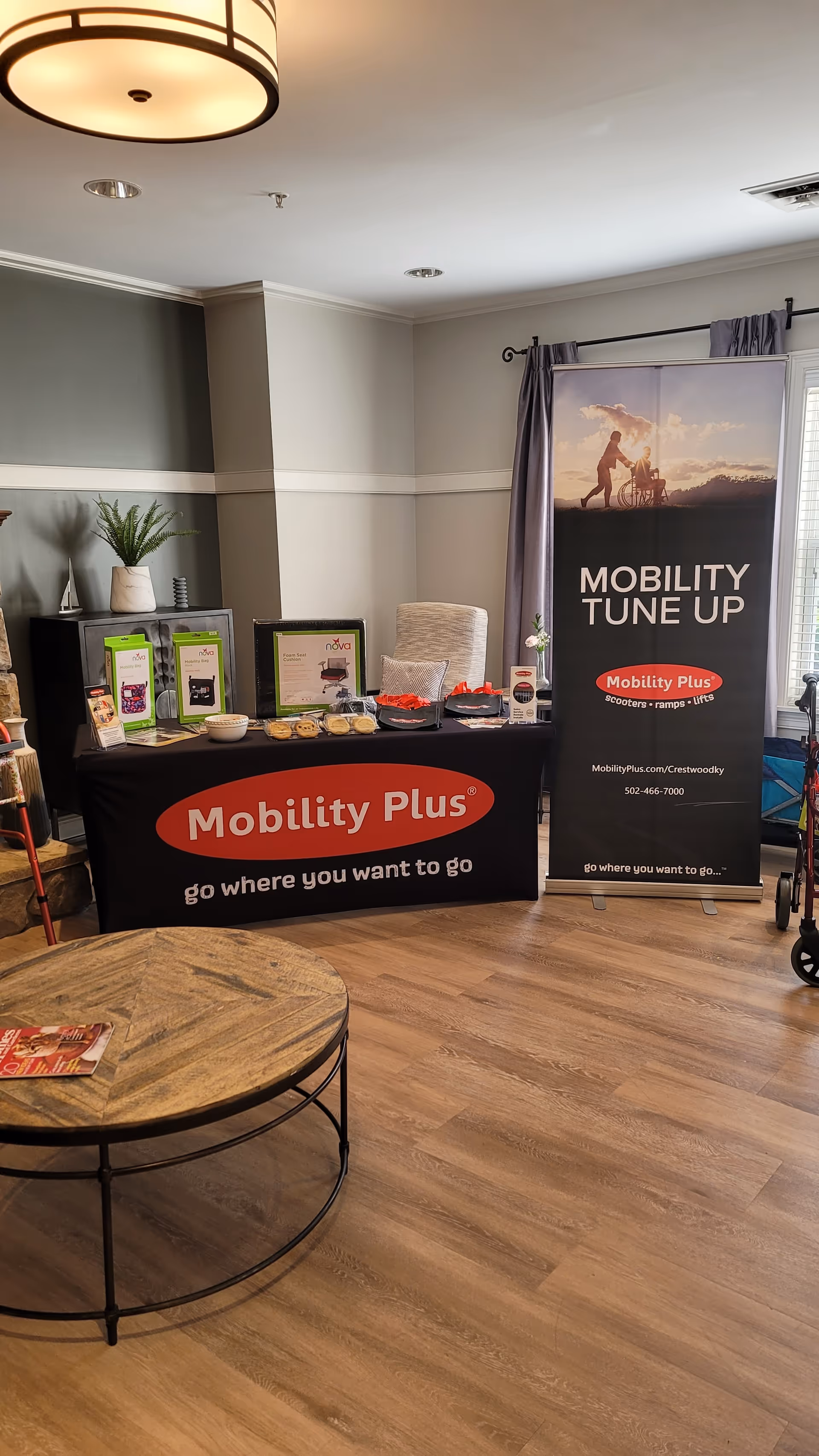 Indoor display setup with Mobility Plus banner, product samples, and a round coffee table.