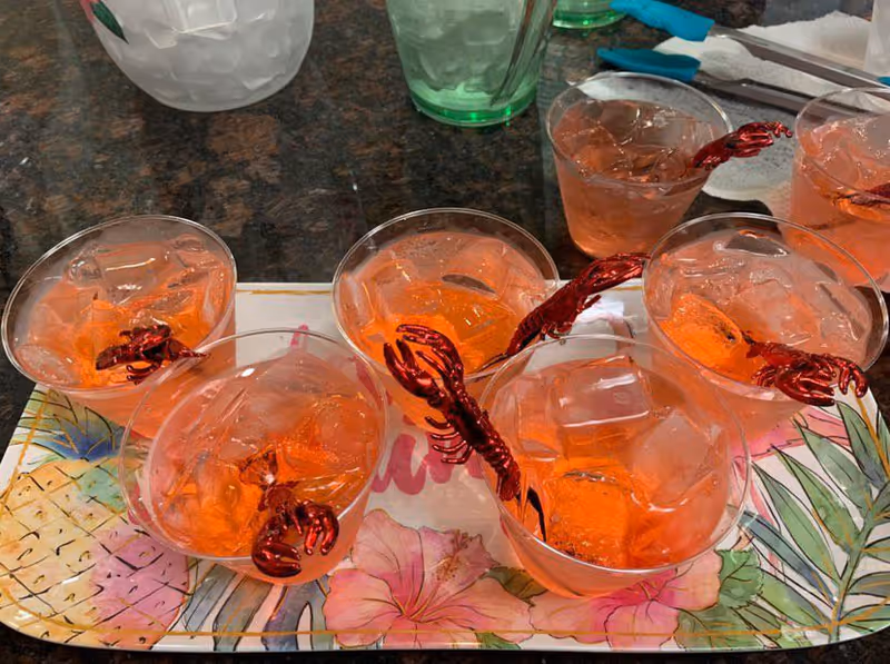Several pink cocktails with ice and red swirl straws sit on a tropical-themed tray.