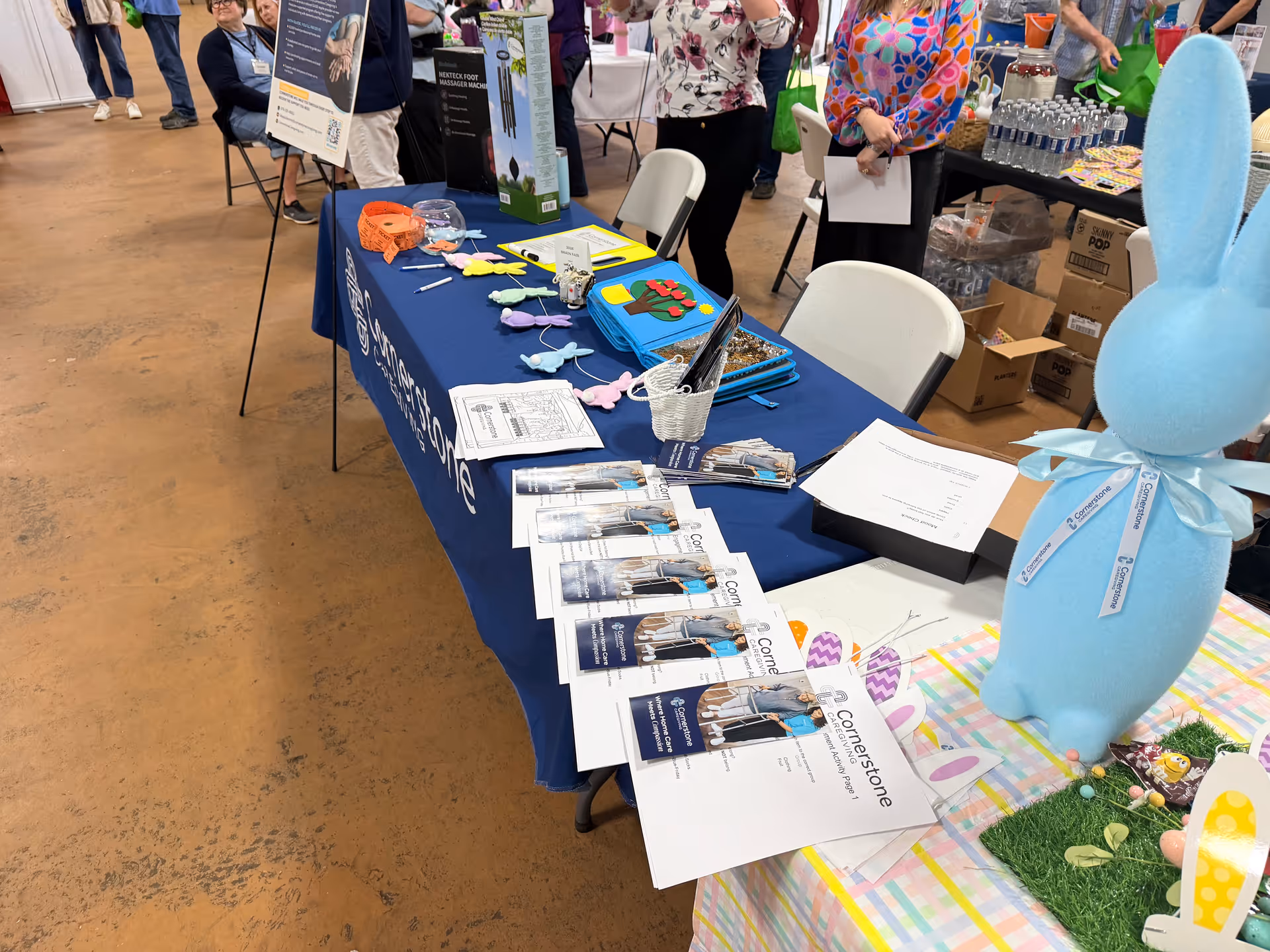 A booth at a senior care fair displays Cornerstone Caregiving brochures and a blue bunny figure.