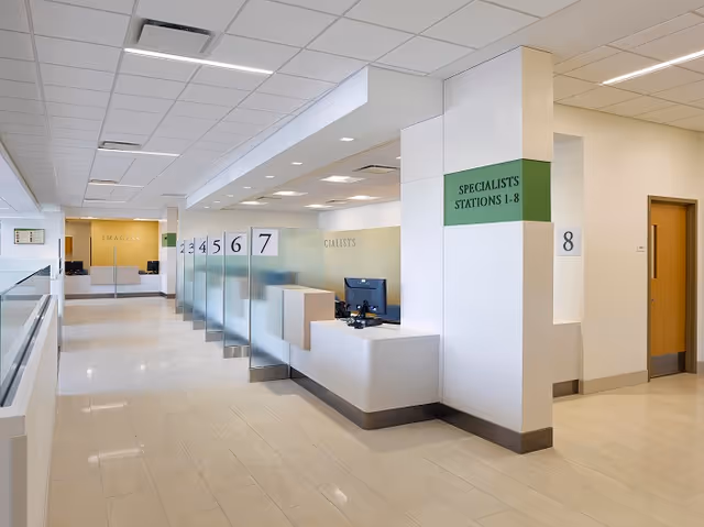 Bright, modern medical reception area with numbered service desks and green specialist signs.
