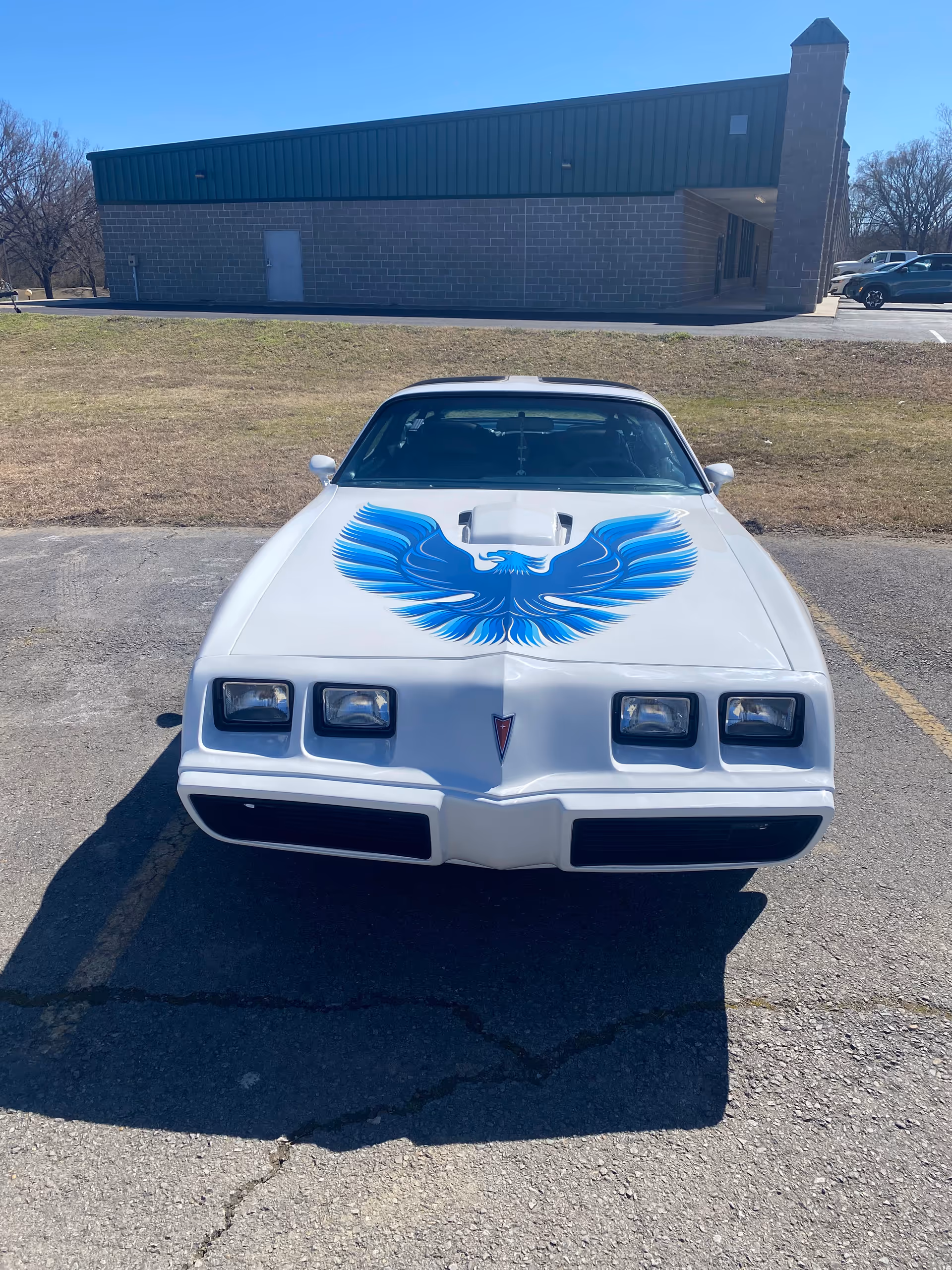 A white classic car with blue eagle hood art parked in a lot near Gentiva Hospice.