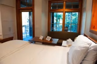 A neatly made bedroom with a bed, bench, and large windows overlooking a balcony.