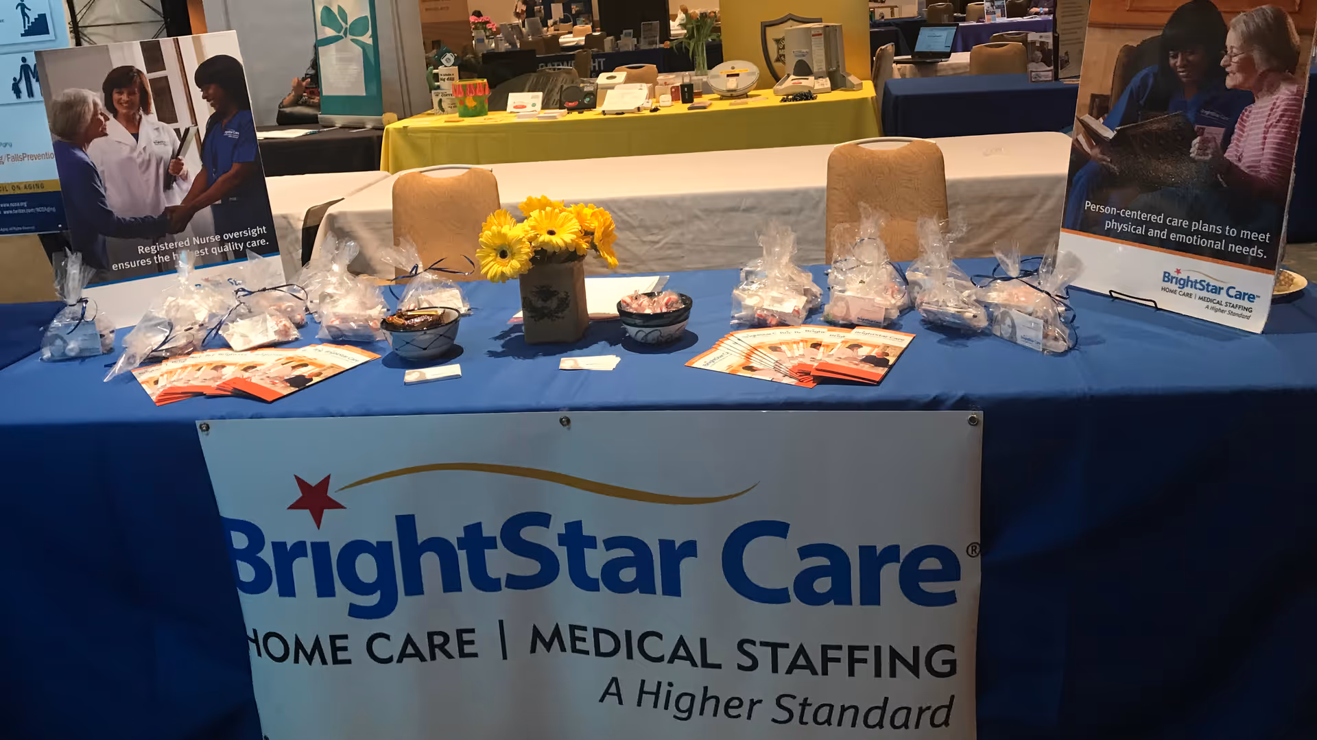 BrightStar Care booth at an expo with banners, brochures, and gift bags on a blue table.