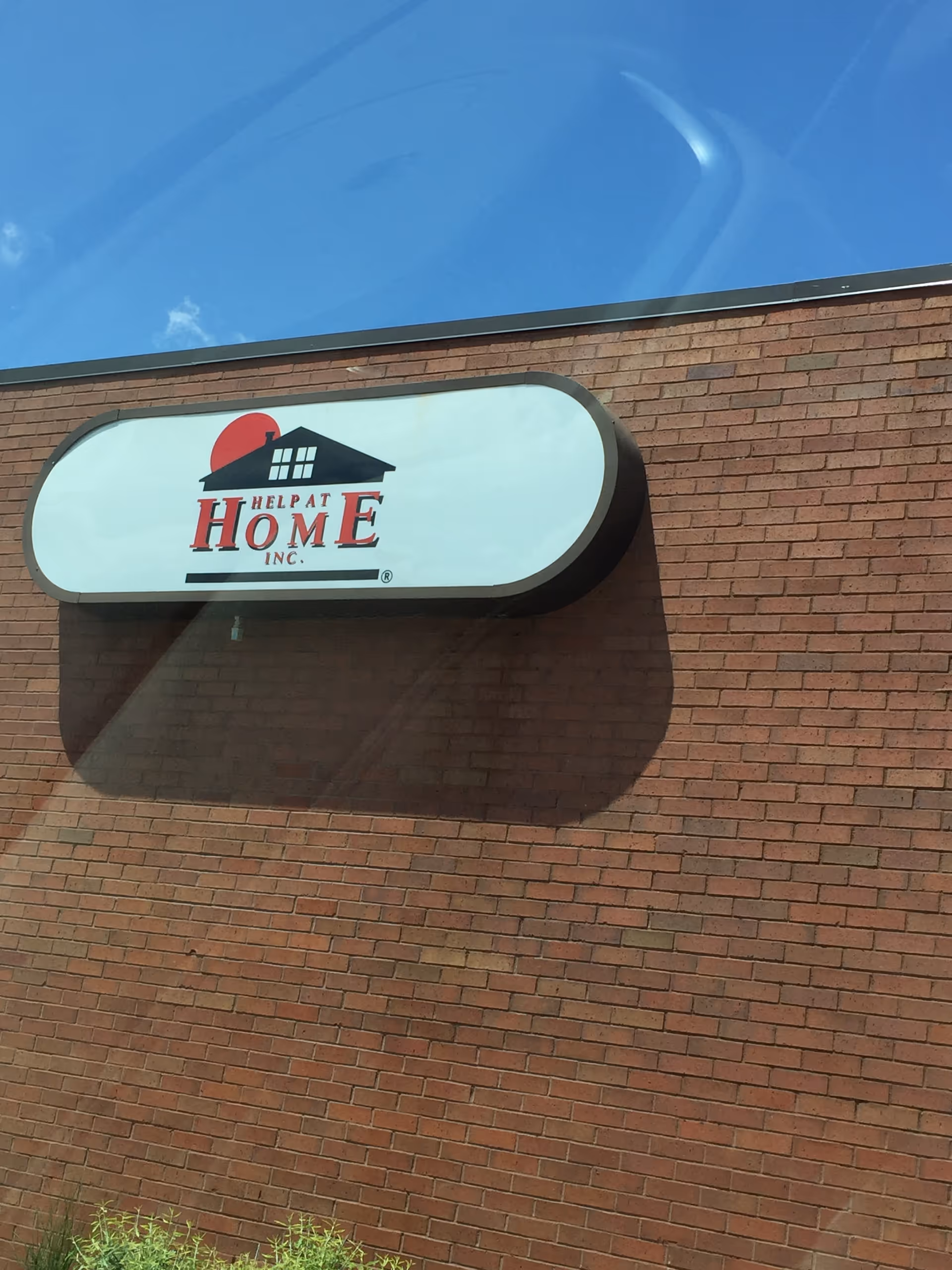 Brick exterior wall with an oval sign displaying Help at Home Inc.