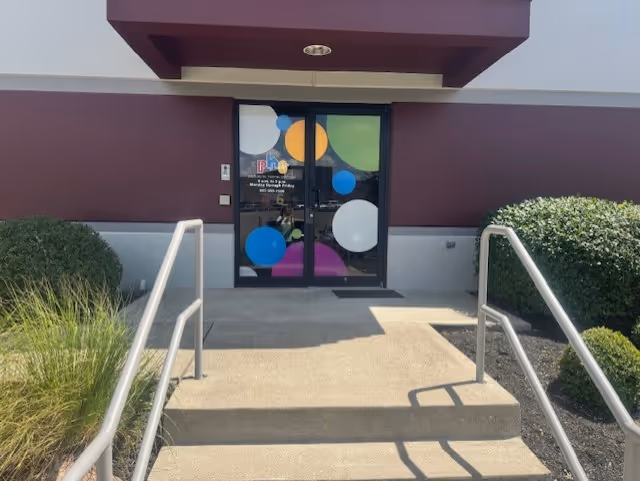 Exterior building entrance with glass doors featuring colorful circle decals, steps, and handrails.